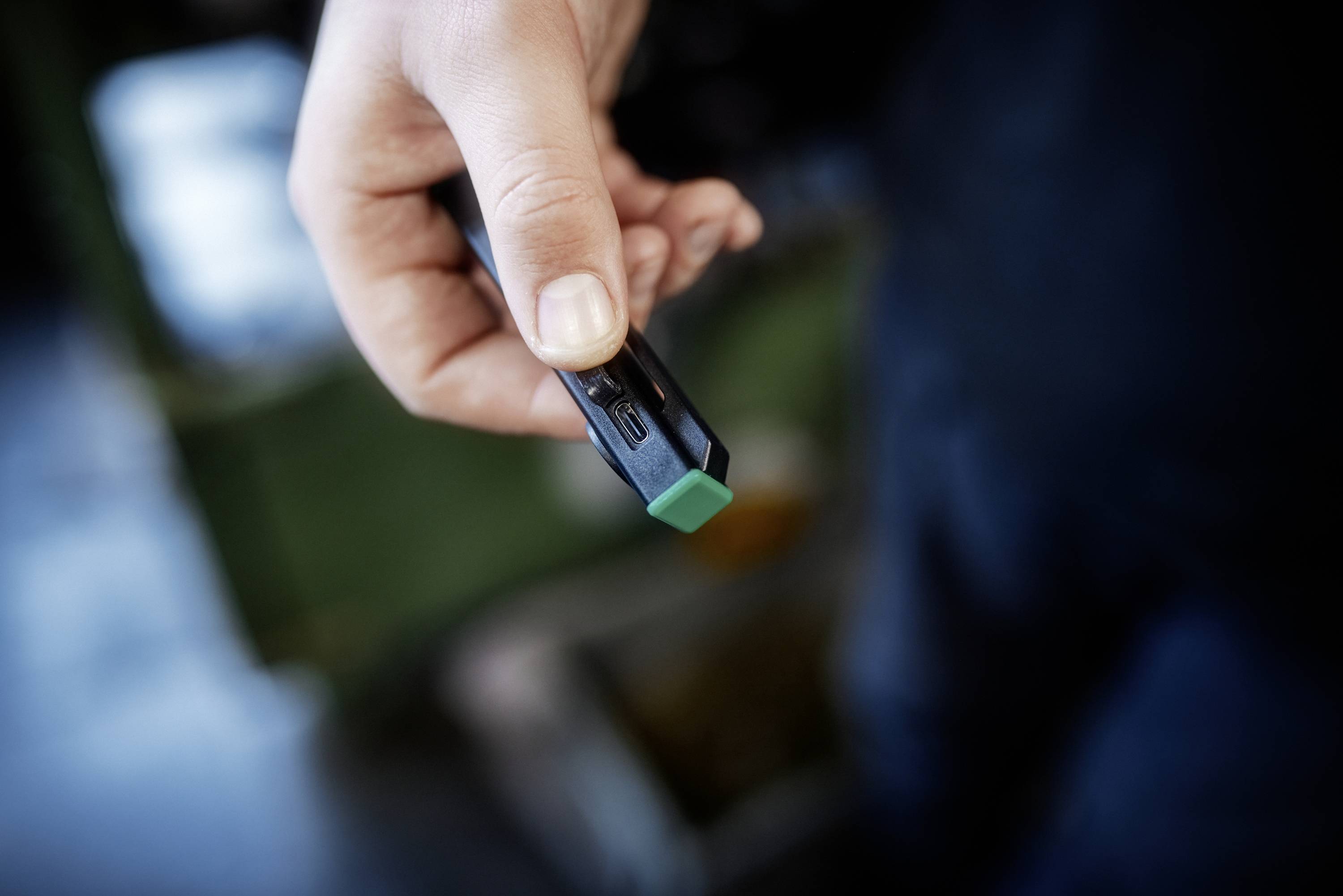Een persoon houdt een zwarte stift met een groene dop vast, gefocust op de hand en het uiteinde van de stift. De achtergrond is wazig, wat wijst op een binnenruimte.