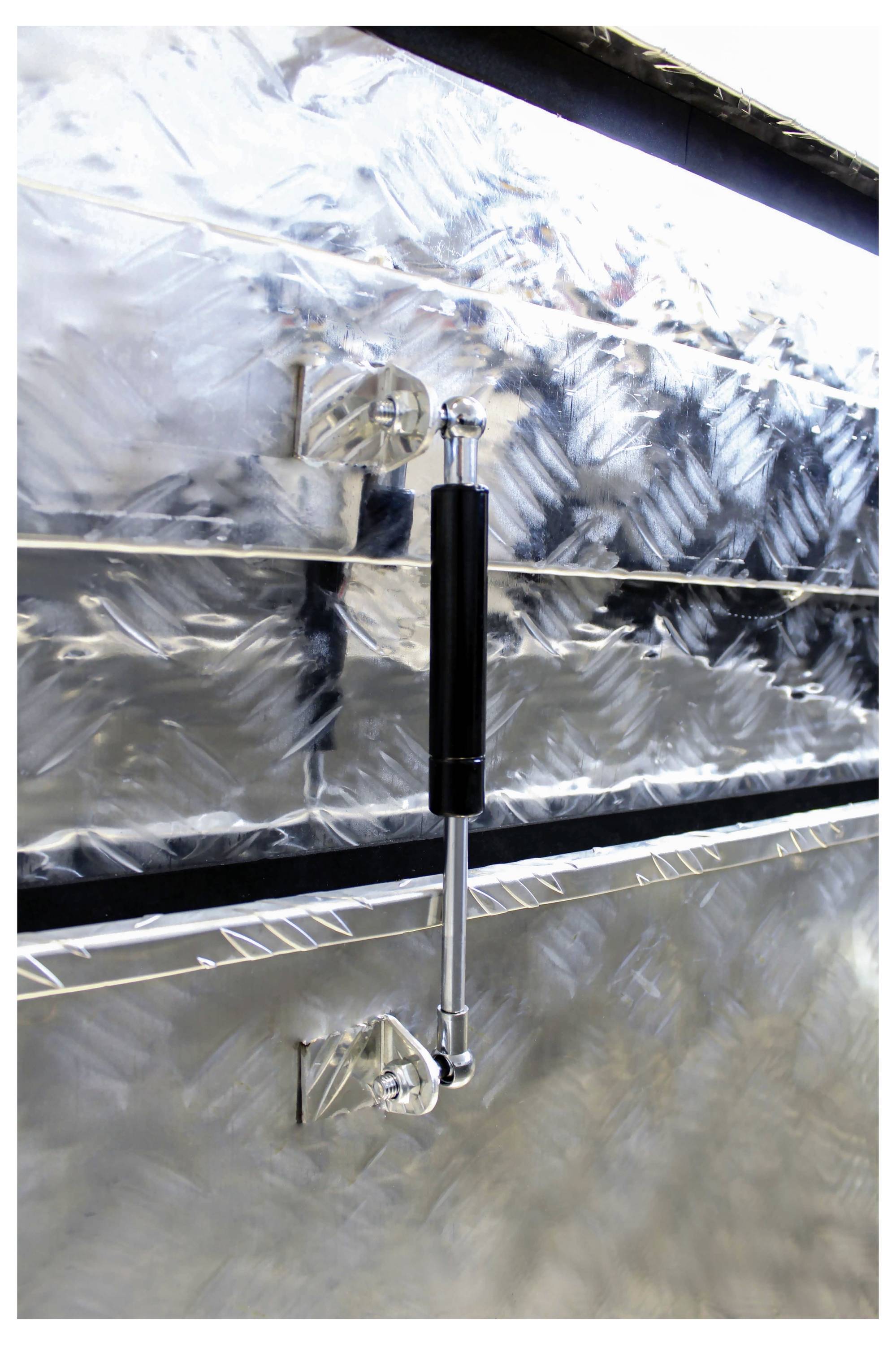 Metalen hydraulische cilinder aan een zilveren industriële behuizing, weerkaatst het licht en onthult mechanische componenten.