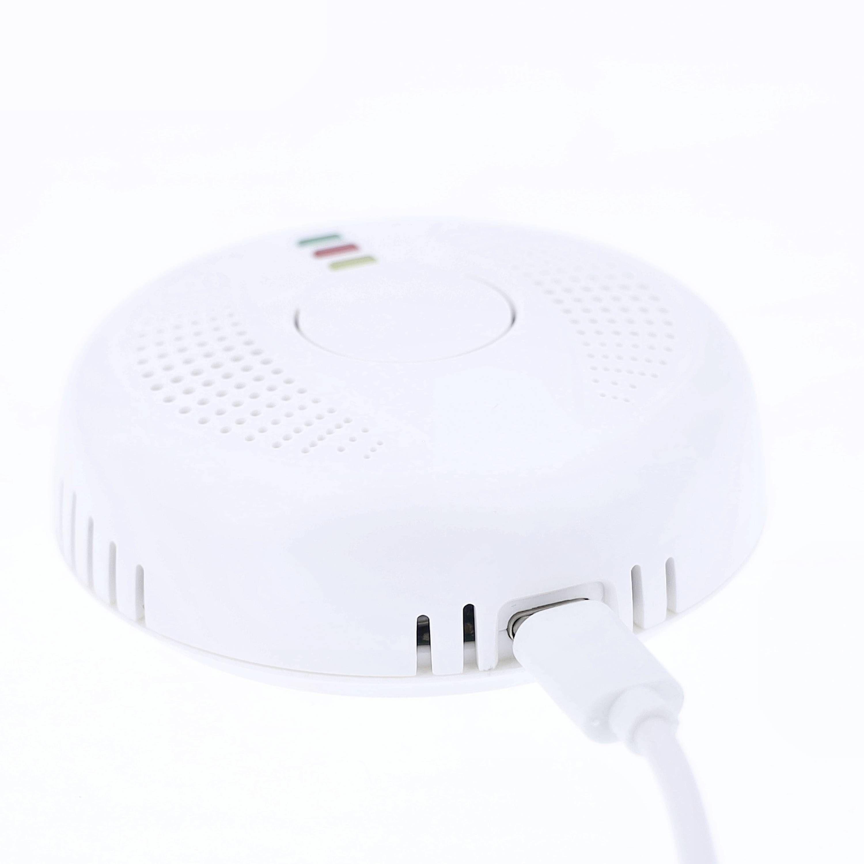 Een witte rookmelder met een aangesloten kabel, toont LED's in rood, groen en geel ter aanduiding van de functie.