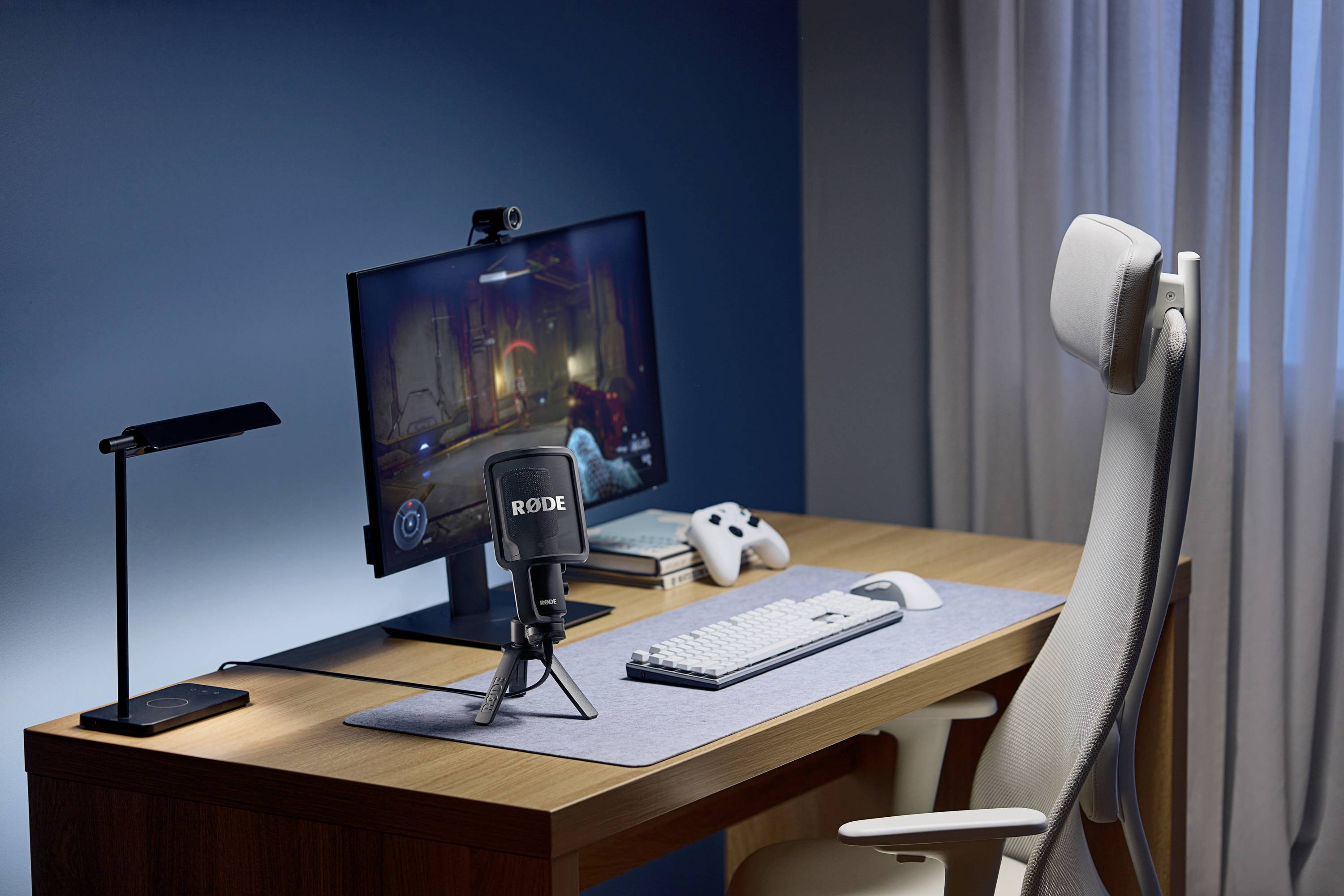 Een moderne bureau met computermonitor, toetsenbord, microfoon, koptelefoon en een controller. Perfect voor gaming of streaming.