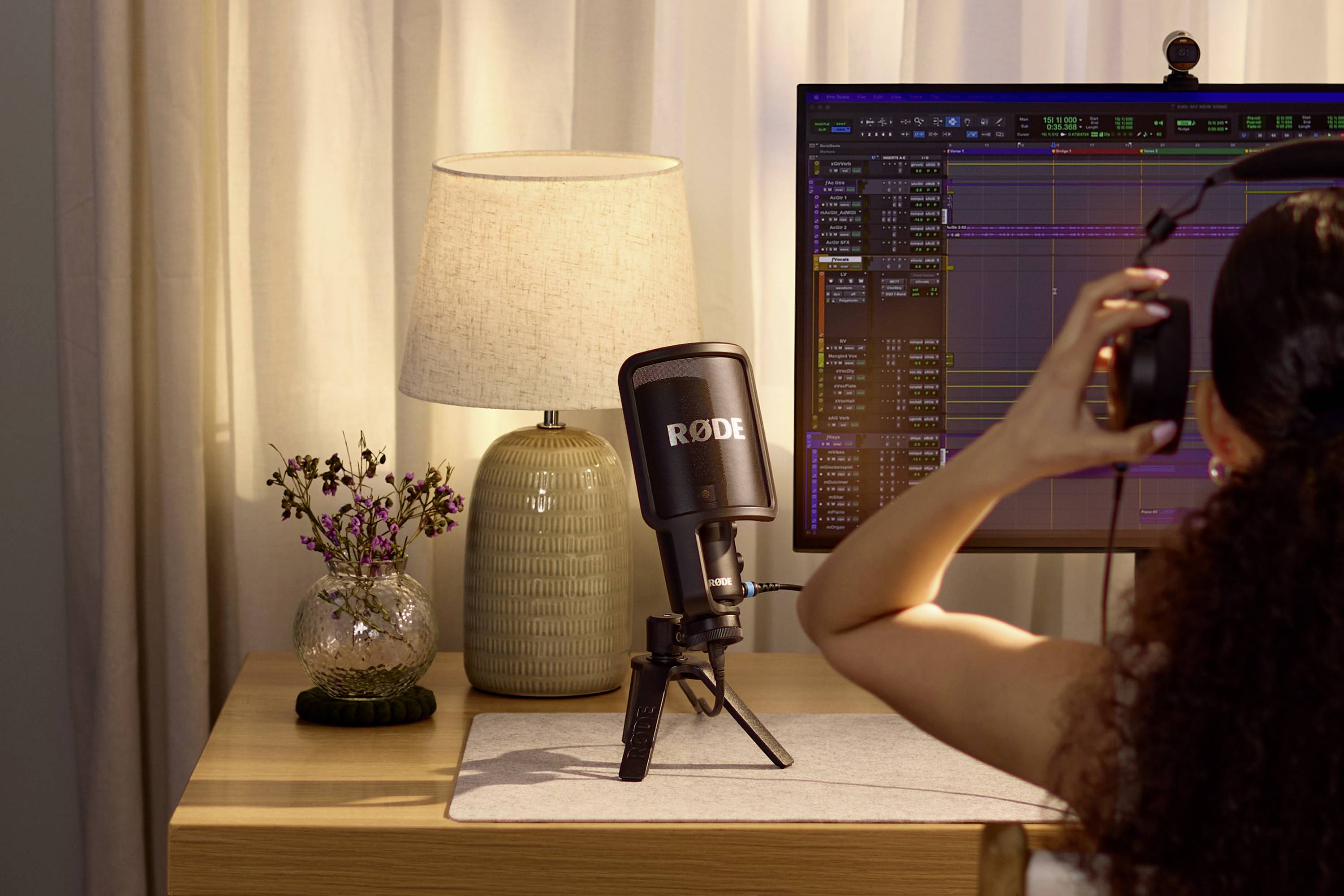 Een persoon gebruikt koptelefoon en microfoon aan een bureau met een computerscherm waarop audioverwerkingssoftware draait.