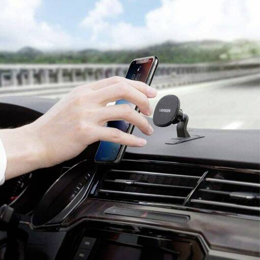 Een hand plaatst een smartphone in een magnetische autohouder op het dashboard van een rijdende auto.