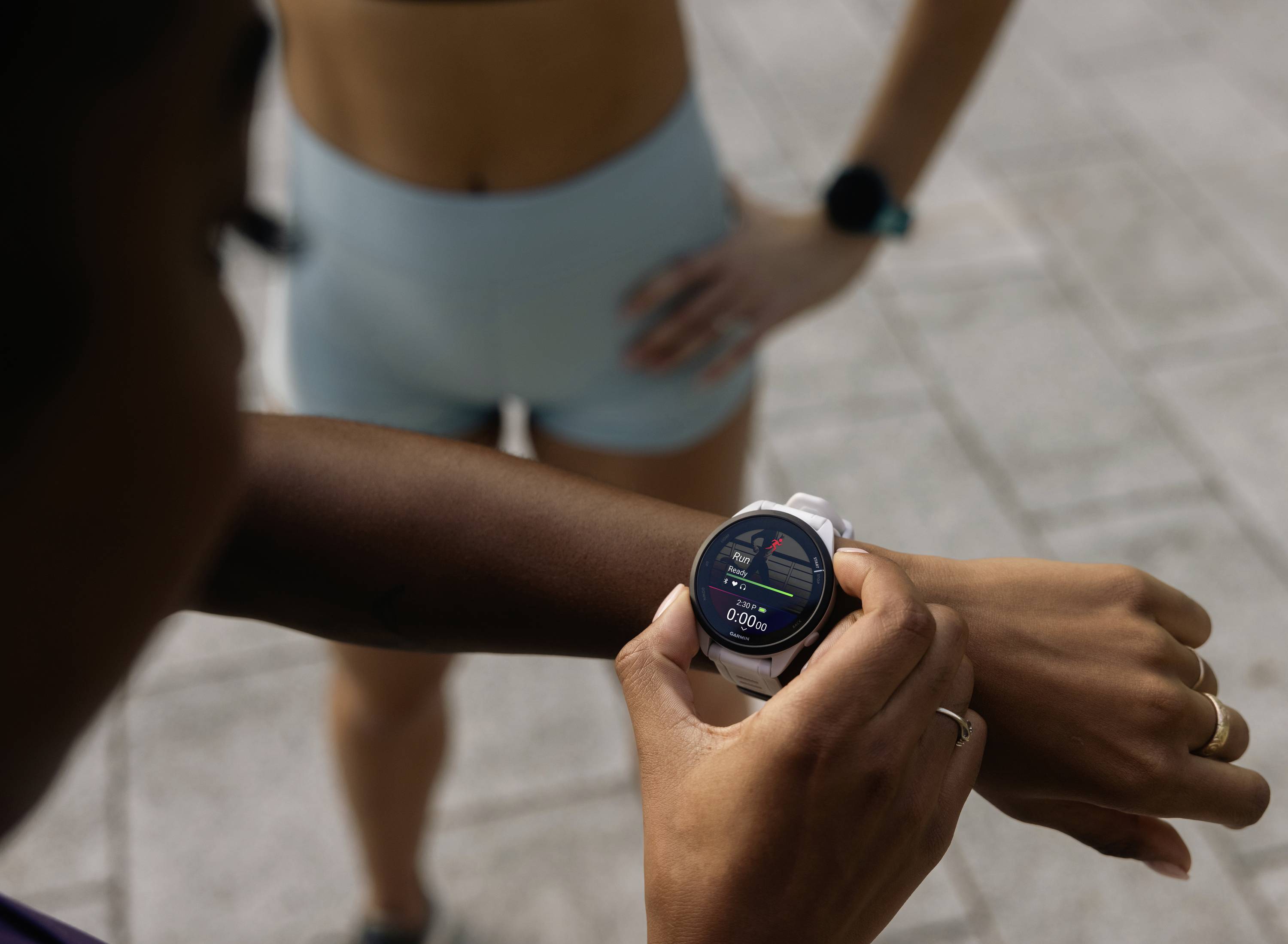 Persoon met smartwatch bewaakt fitnessgegevens; tweede persoon op de achtergrond in sportkleding. Hoofdfocus op techniek in sport.
