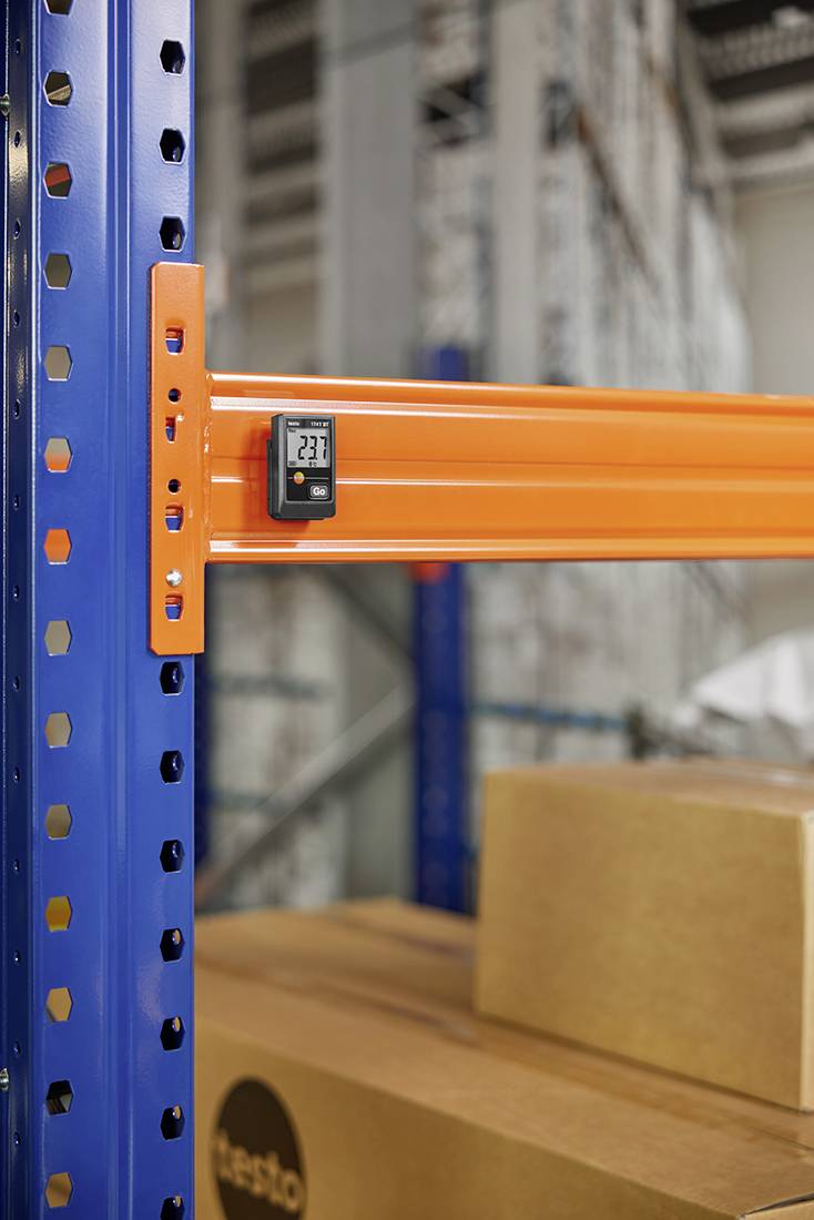 Rek in het magazijn met een oranje balk en een digitaal thermometer dat 23,1 graden aangeeft. Dozen zijn eronder zichtbaar.