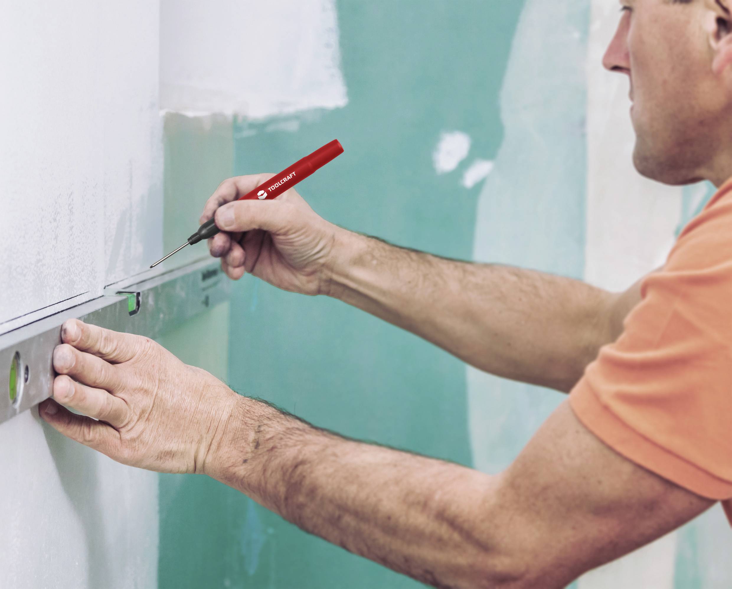 Een man meet met een waterpas en markeert een lijn op de muur.