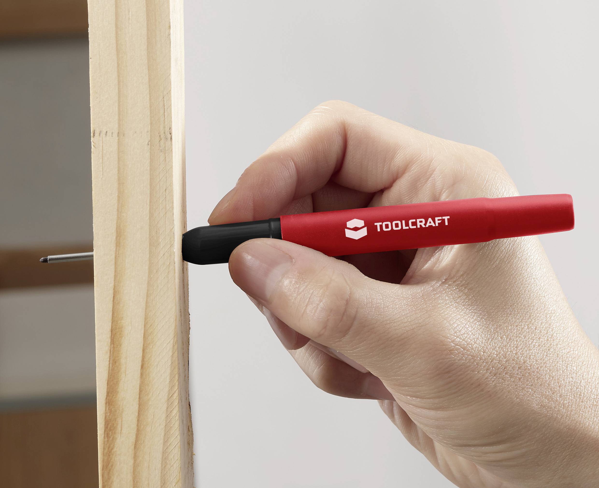 Een hand houdt een rode Toolcraft-pen vast om een markering op een stuk hout te maken.
