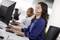 Een vrouw en een man werken op computers in een kantoor. Beiden dragen headsets en glimlachen terwijl ze naar hun schermen kijken.