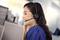 Vrouw met headset zit glimlachend voor een computerscherm, terwijl ze met een klant in gesprek is. Kantooromgeving op de achtergrond.