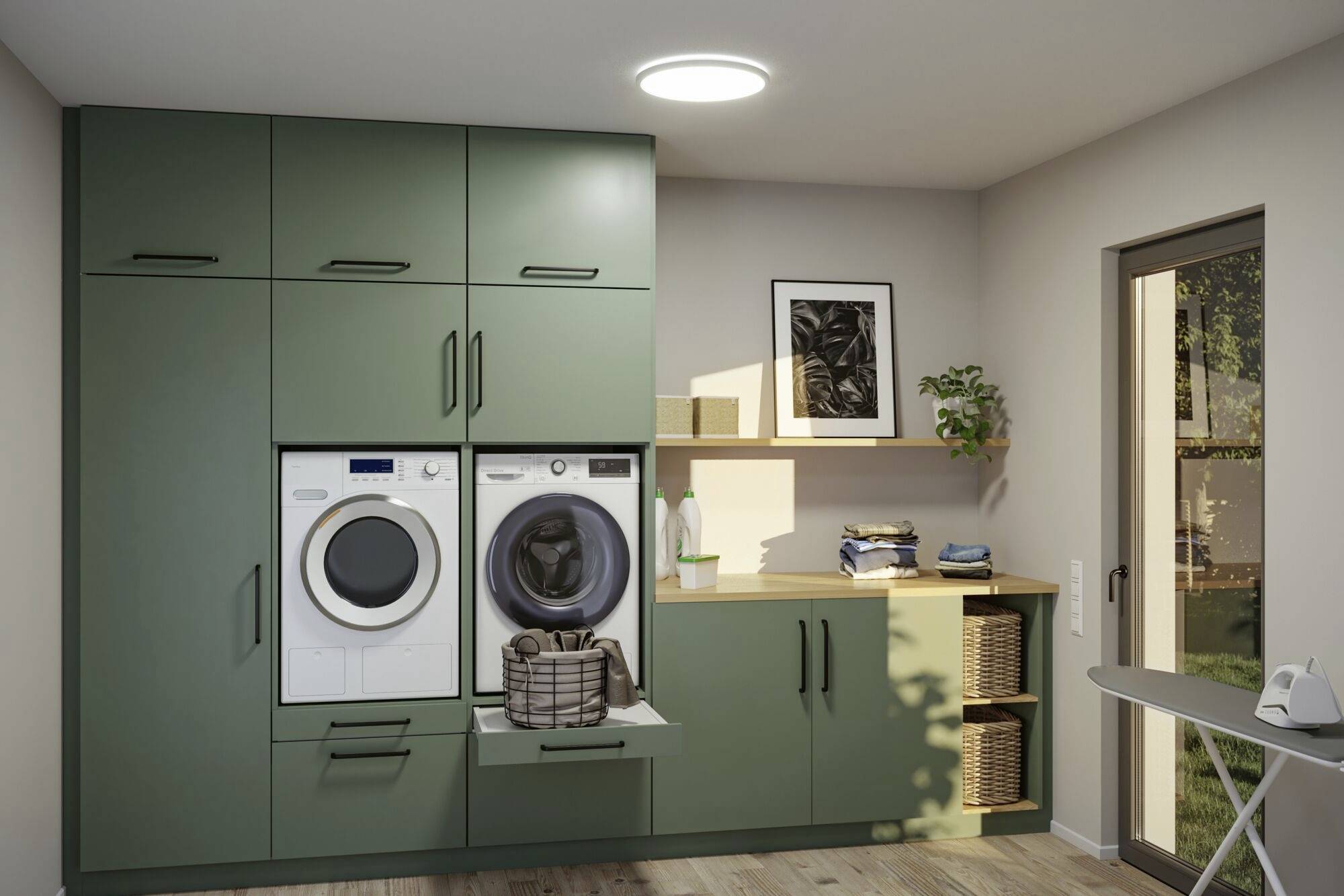 'Modern ingerichte bijkeuken met groene kasten, open opbergruimte, wasmachine en droger. Strijkplank rechts.'