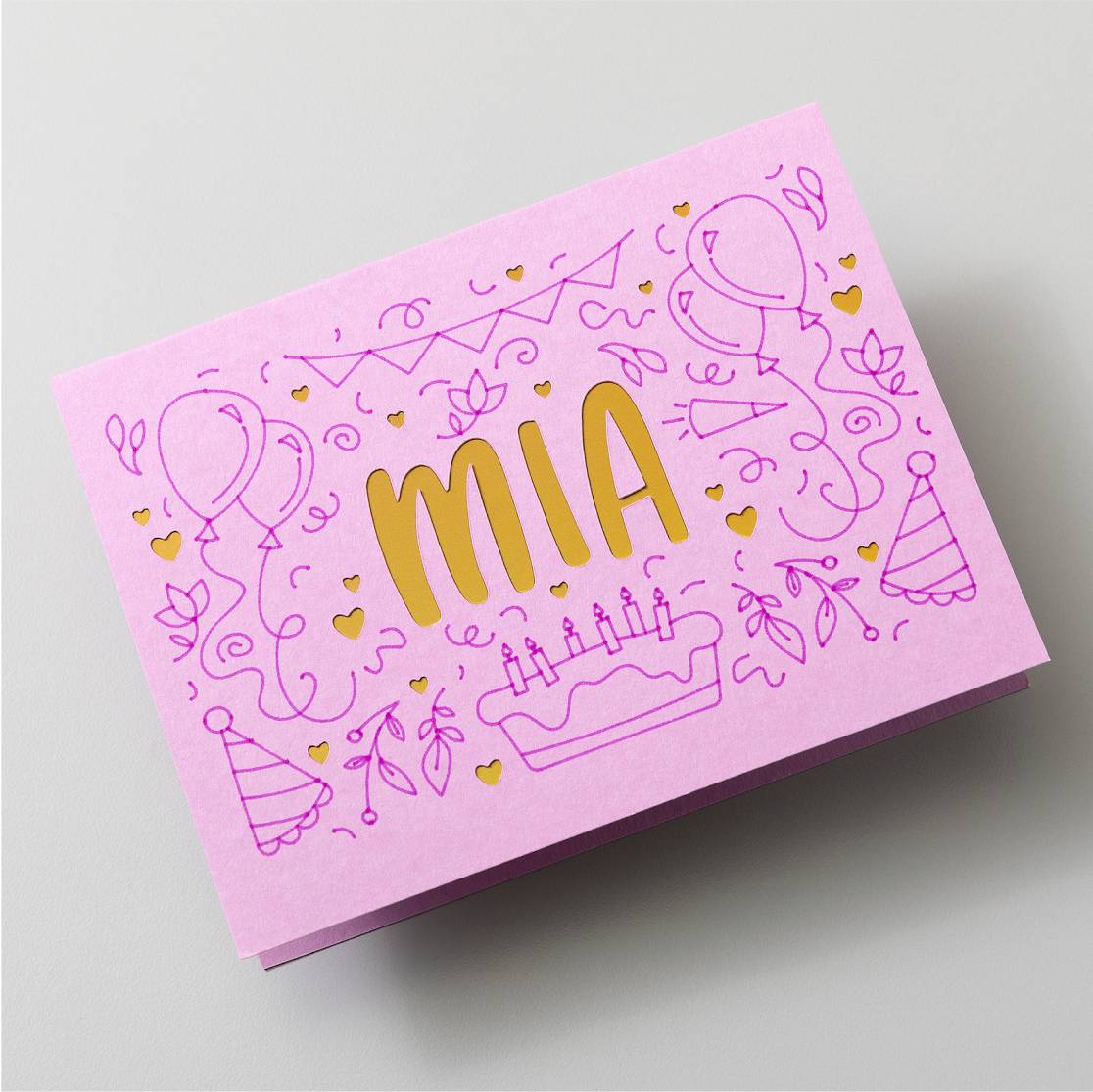 Roze verjaardagskaart met gouden opschrift 'Mia'. Omringd door illustraties van ballonnen, taart en feesthoedjes.