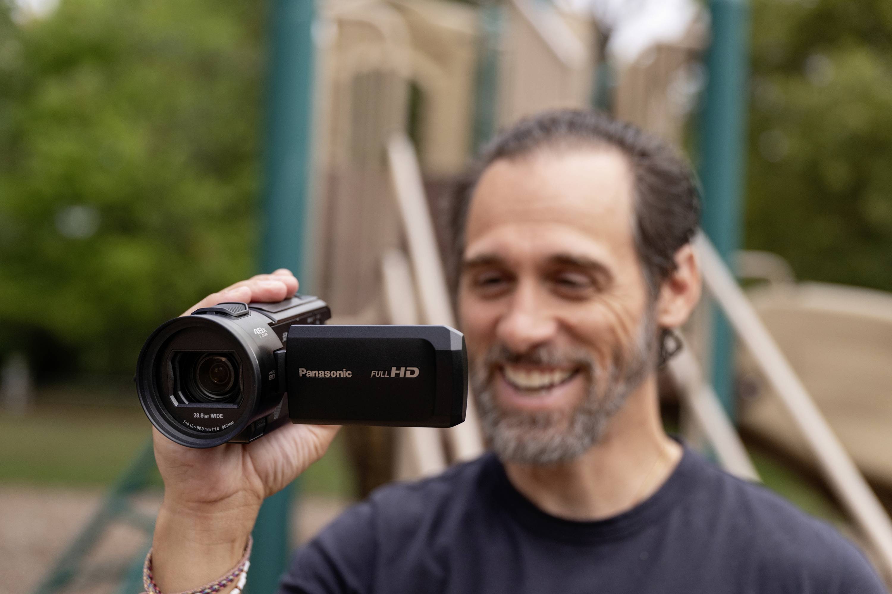 Een man filmt buiten met een Panasonic Full HD-videocamera. Op de achtergrond is een onscherpe speeltuin te zien.