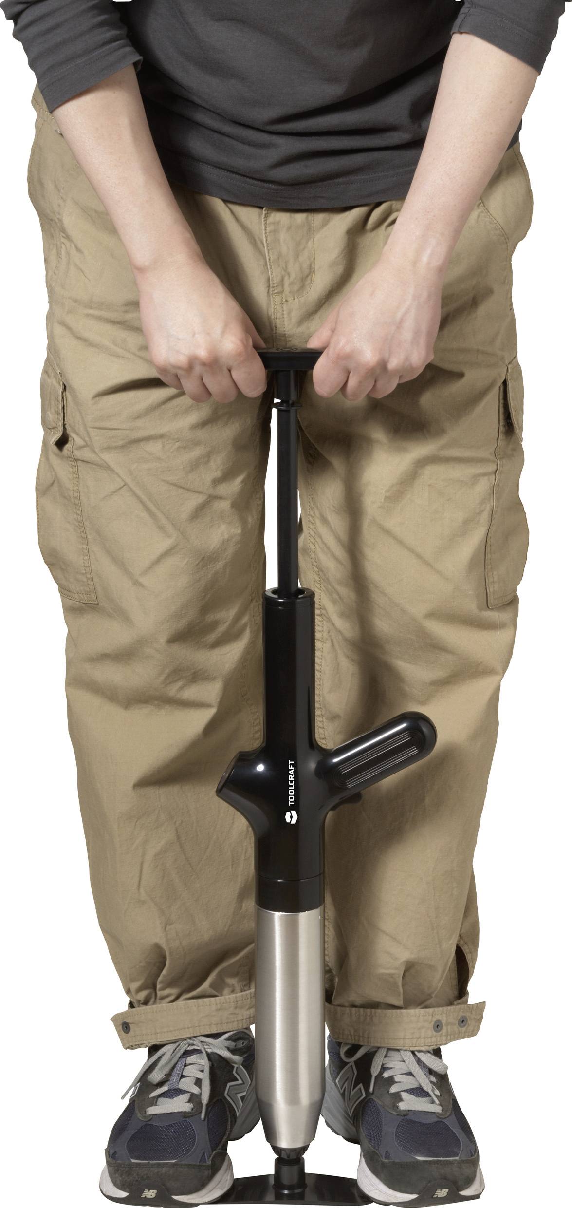 Een persoon pompt lucht met een handpomp. Ze draagt beige broeken en sportschoenen.