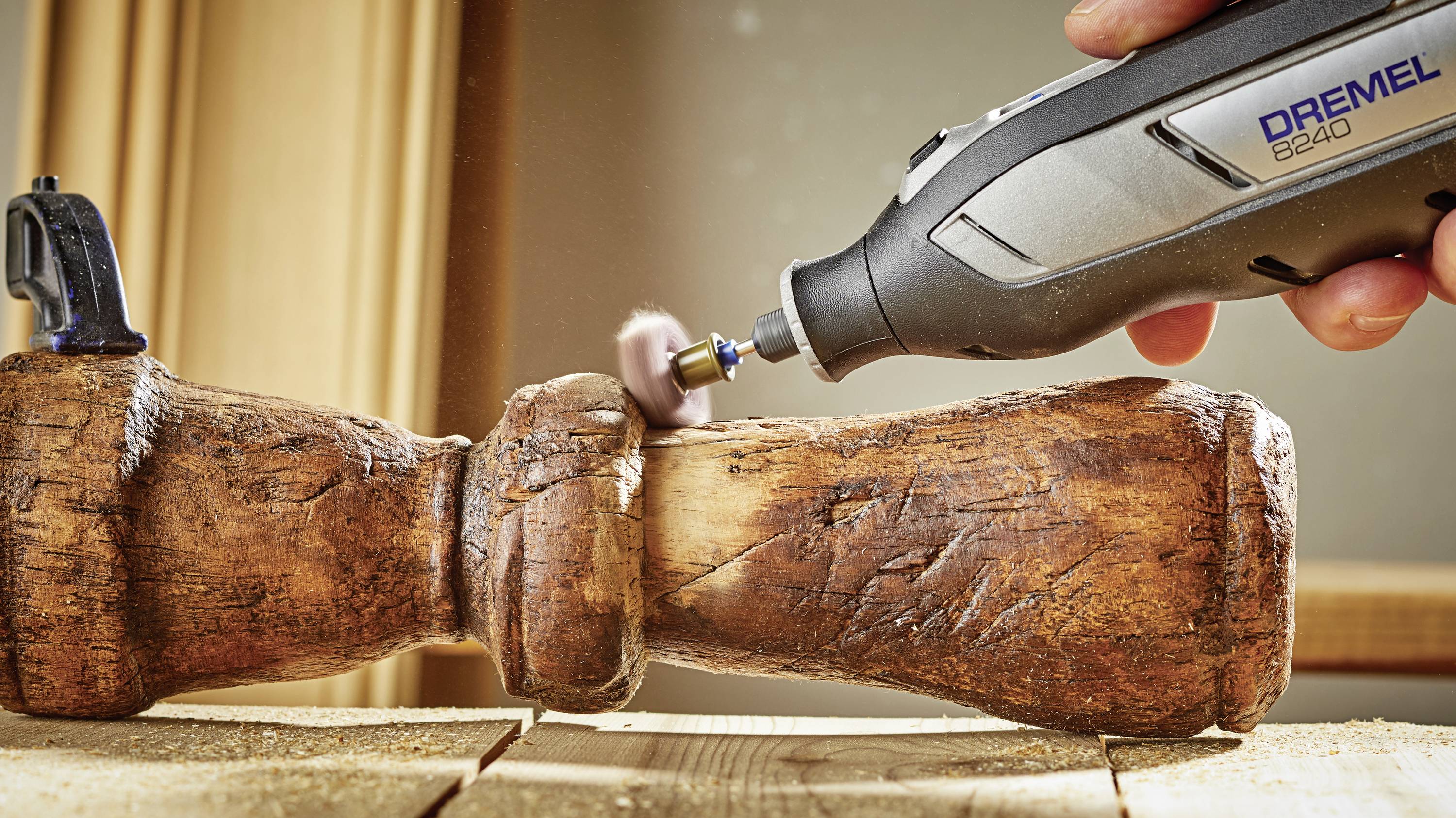 'Close-up: Een hand slijpt een houten object met een multifunctioneel gereedschap. Houtkrullen en stof zweven in de lucht.'