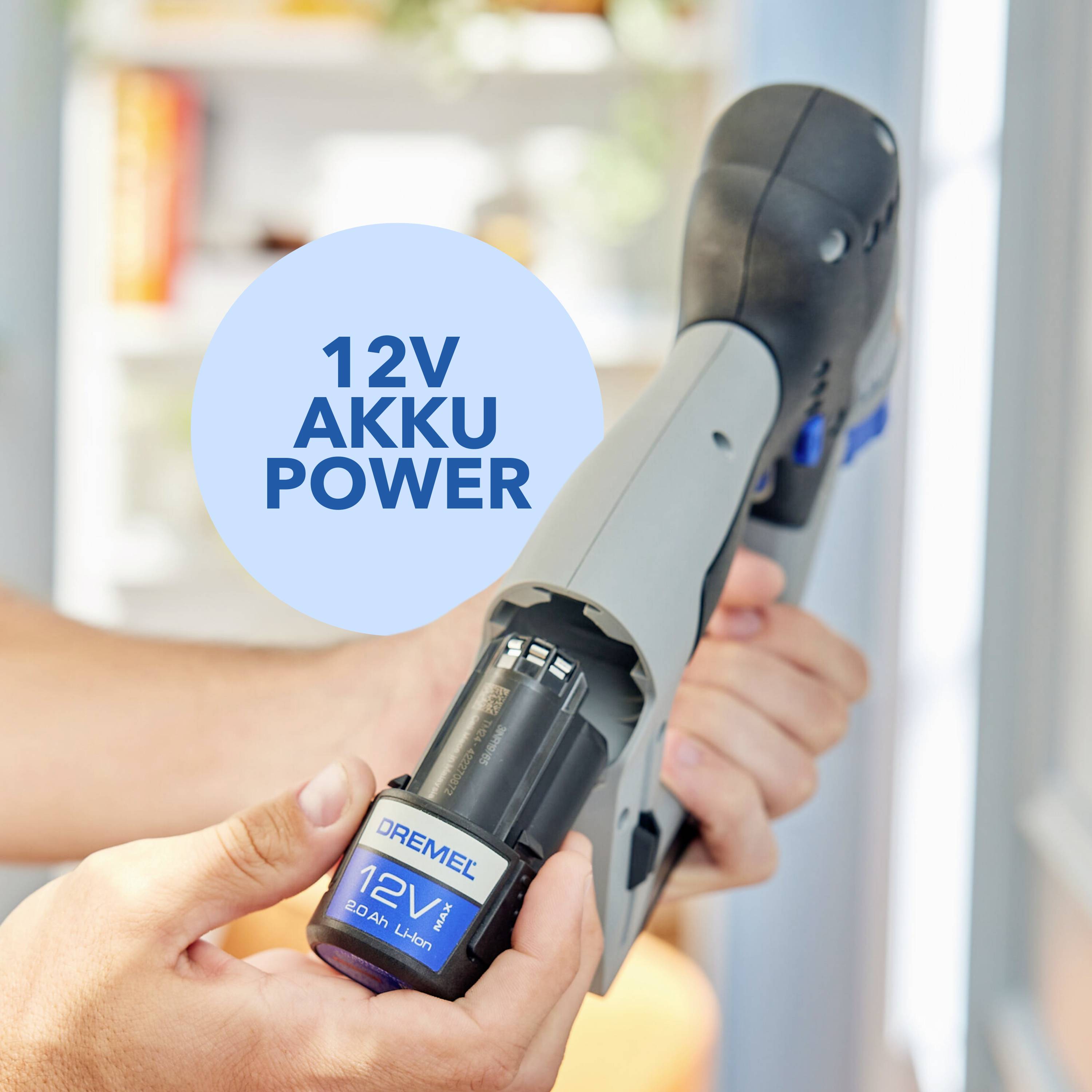 Een hand houdt een 12V Dremel-gereedschap vast met een geplaatste accu; een blauwe cirkel op de bovenkant bevat de tekst '12V Accu Power'.