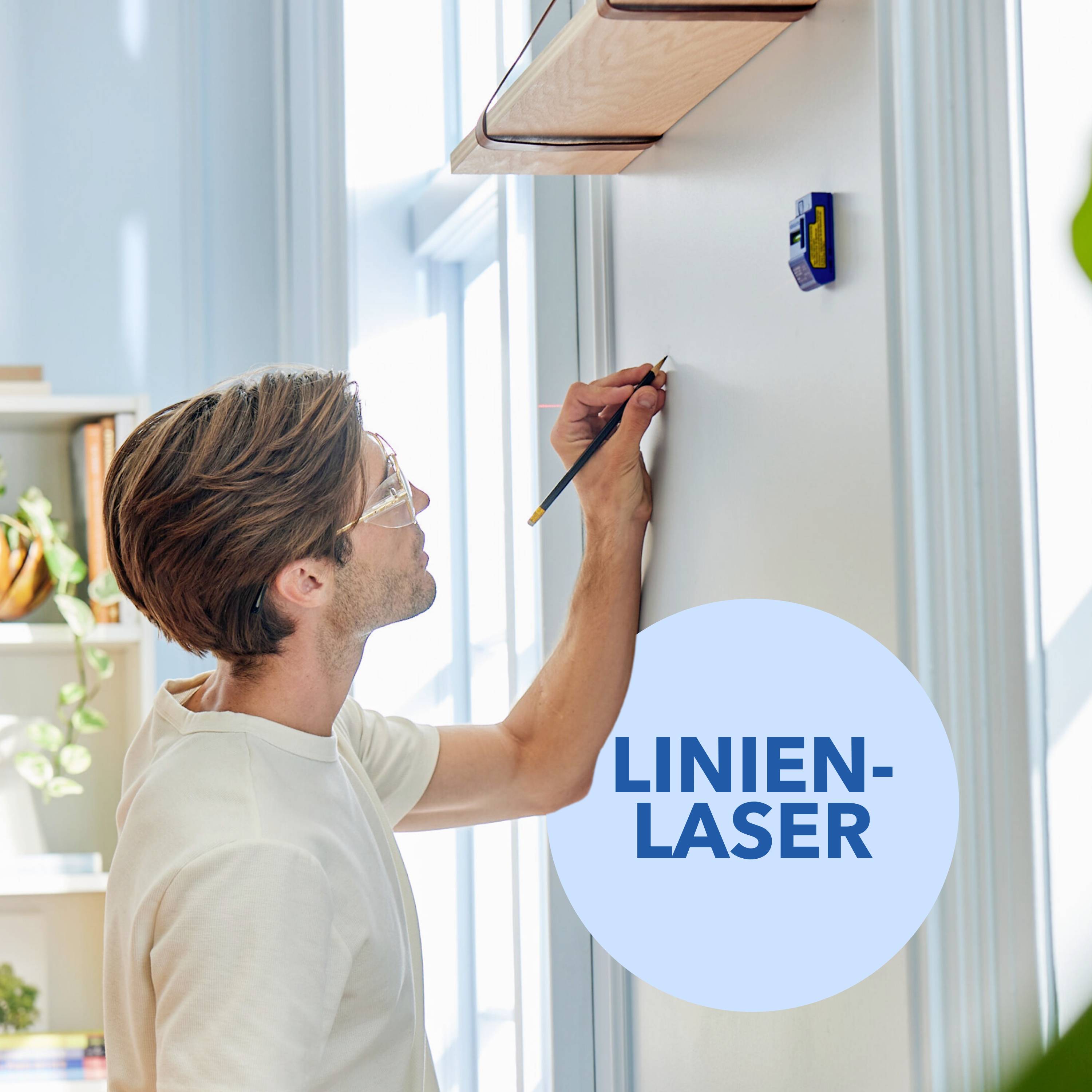 Een persoon gebruikt een lijnlaser om een rechte lijn op een muur te tekenen. Op de achtergrond zijn boekenkasten zichtbaar.