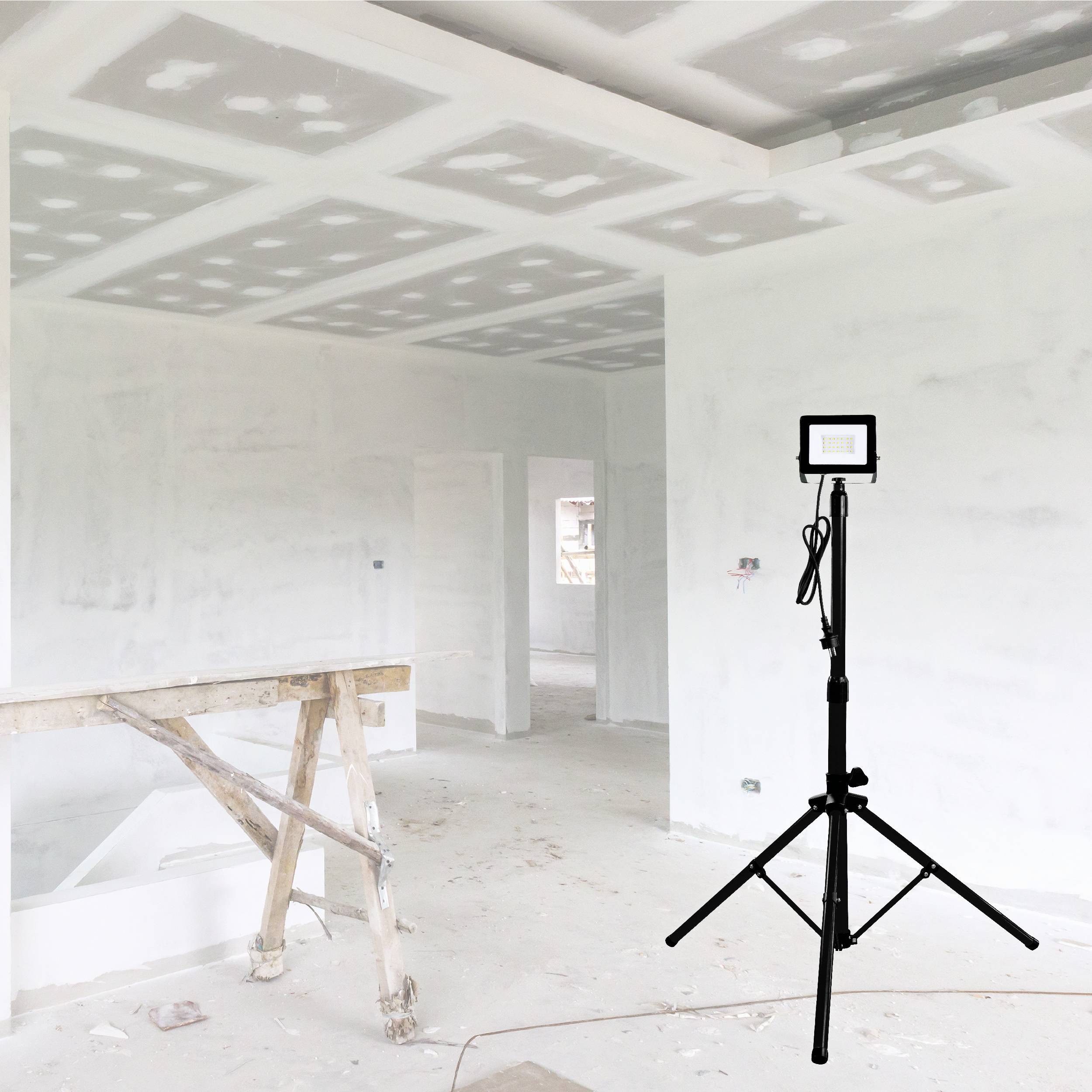 Een lege ruimte in renovatie met verlaagd plafond en een bouwlamp op een statief. Links een steiger; muren pas geplamuurd.