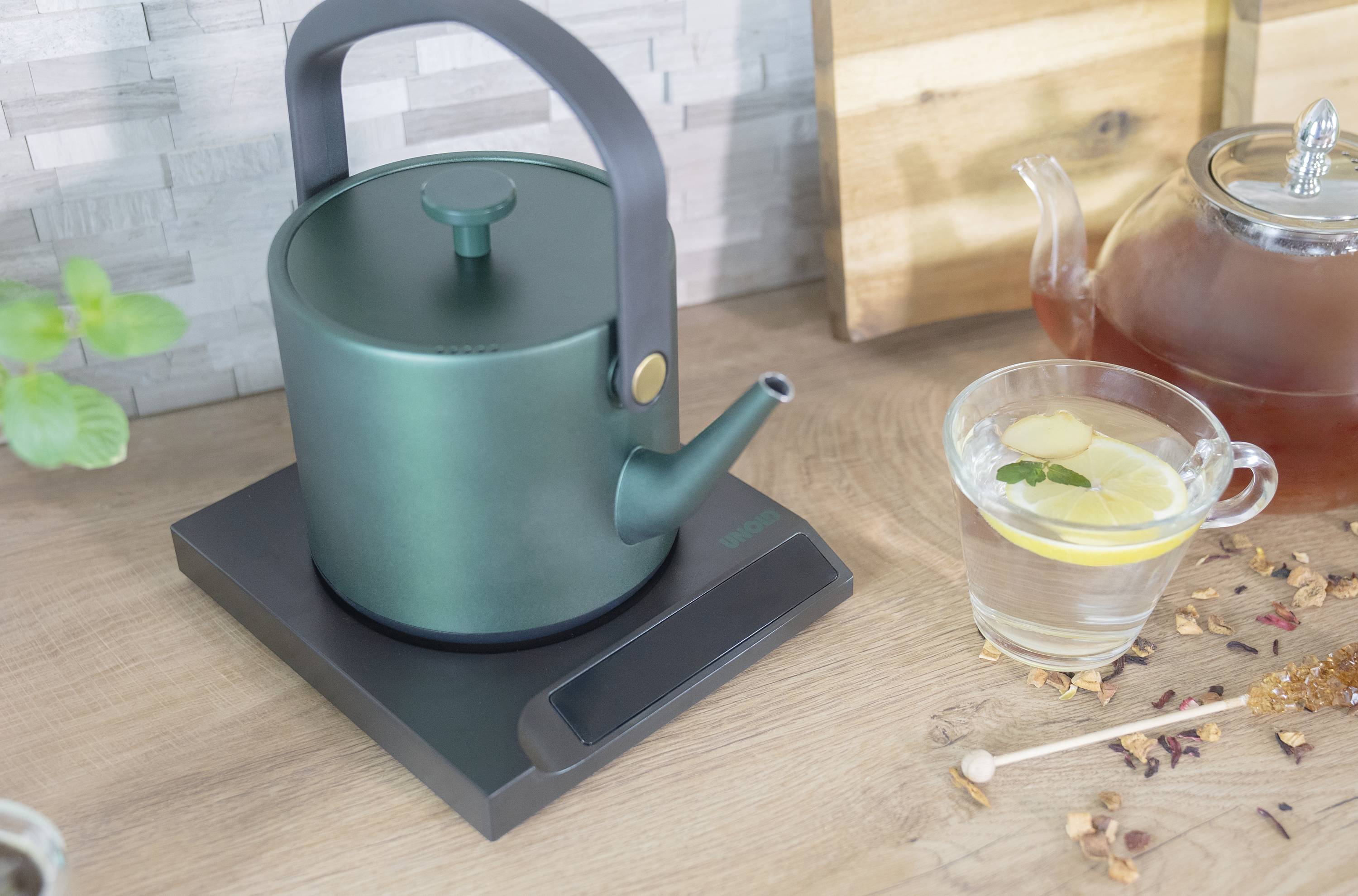 Groene waterketel op fornuis met theepot, glas water, citroen en munt, houten achtergrond.