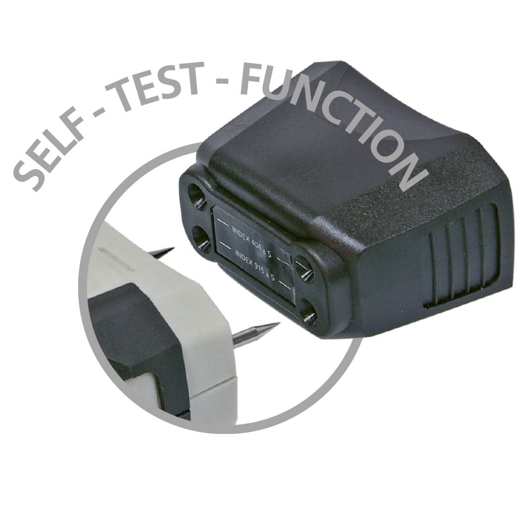 Een zwart apparaat met de opschrift 'SELF-TEST-FUNCTION' toont twee metalen pinnen aan de onderkant, die dienen voor functiecontrole.