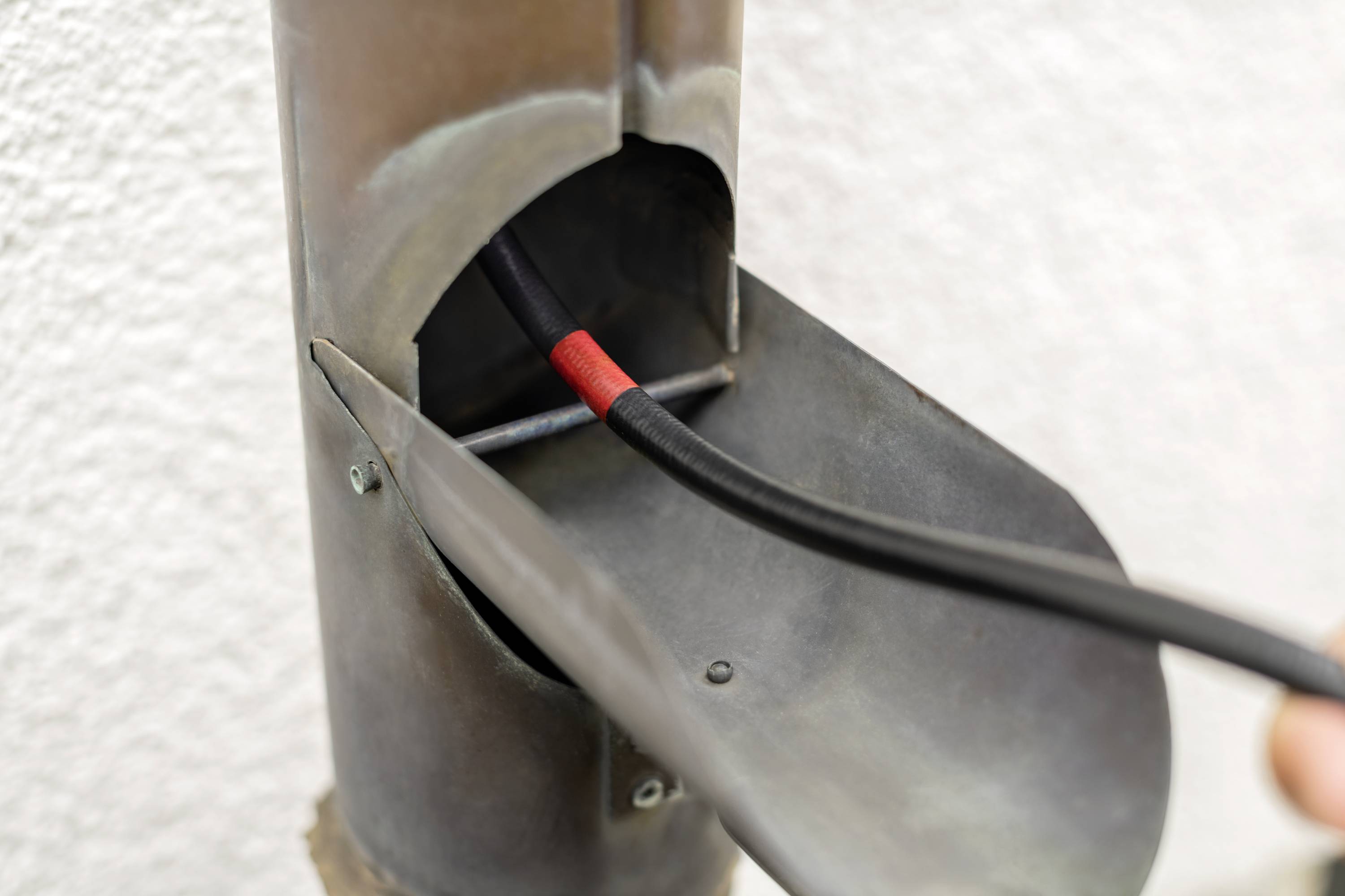 Een buisvormig metalobject dat een zwart, rood gemarkeerd kabel bevat dat door een opening loopt.