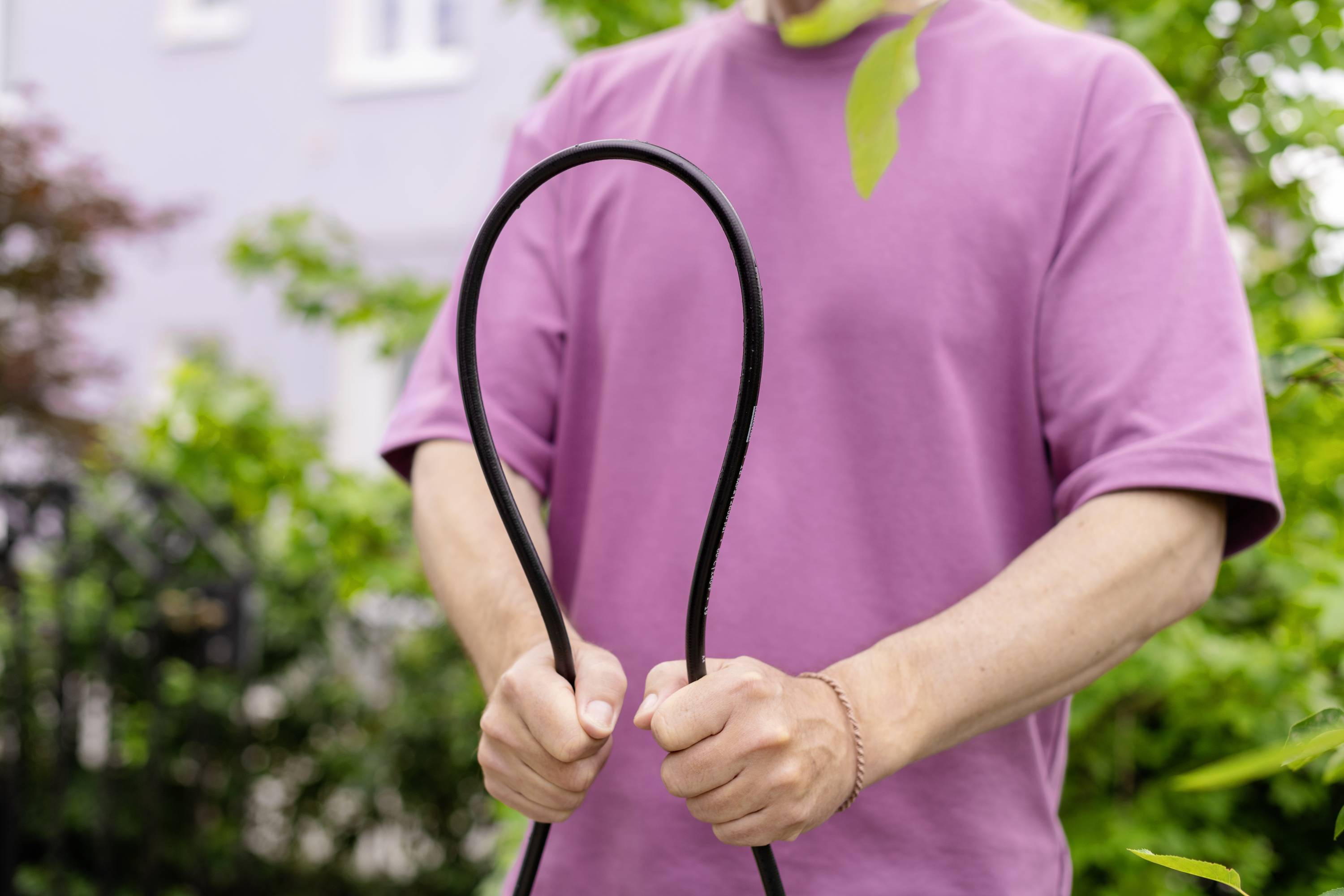 Persoon in een roze T-shirt houdt een zwarte slang vast die is gevormd tot een lus, in de buitenlucht. Op de achtergrond zijn planten zichtbaar.