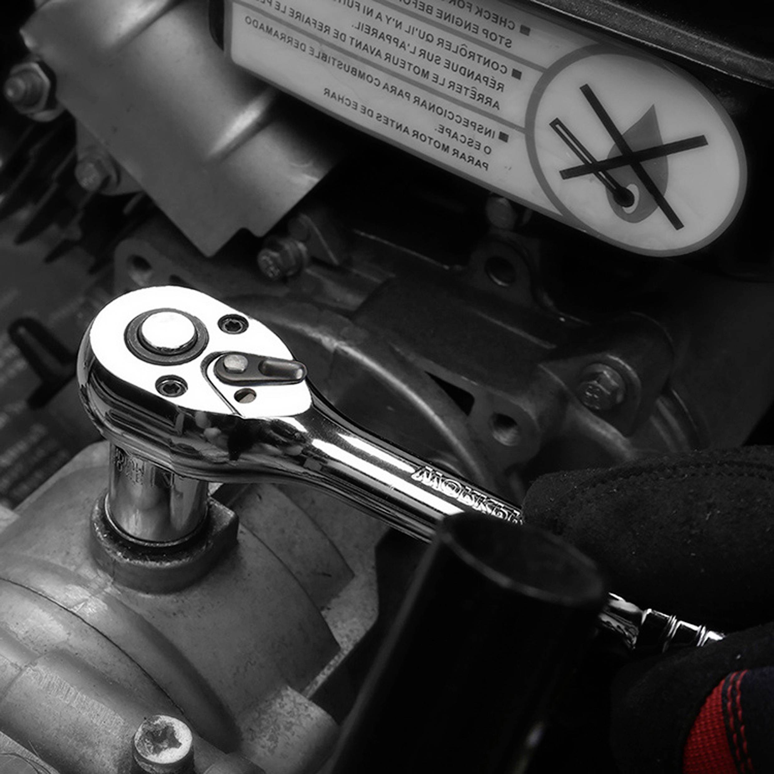 Een persoon gebruikt een ratelsleutel om een onderdeel van een motor af te stellen, met boven een veiligheidswaarschuwingsbord dat een hand en een gekruiste moersleutel toont.