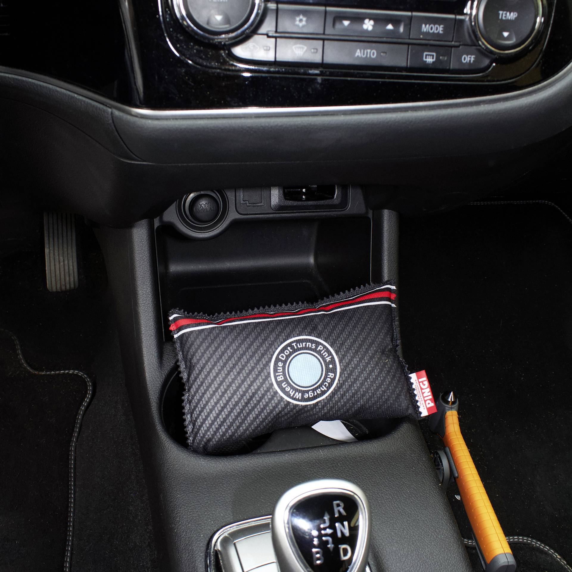 Interieur van een auto met een versnellingspook in het midden en een geurzakje met 'Verwijder Geur' opschrift in het opbergvak.