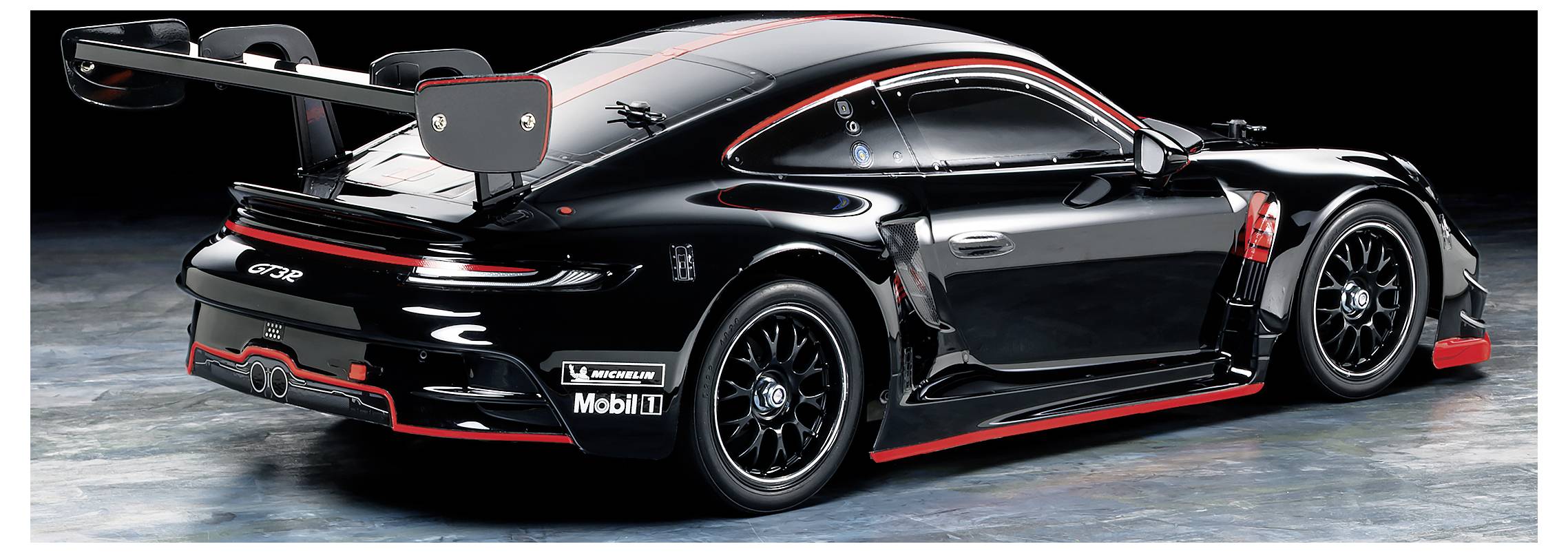 Een zwart racevoertuig met rode accenten, bekeken van achteren. Het heeft een grote achterspoiler en sponsorstickers aan de zijkanten.