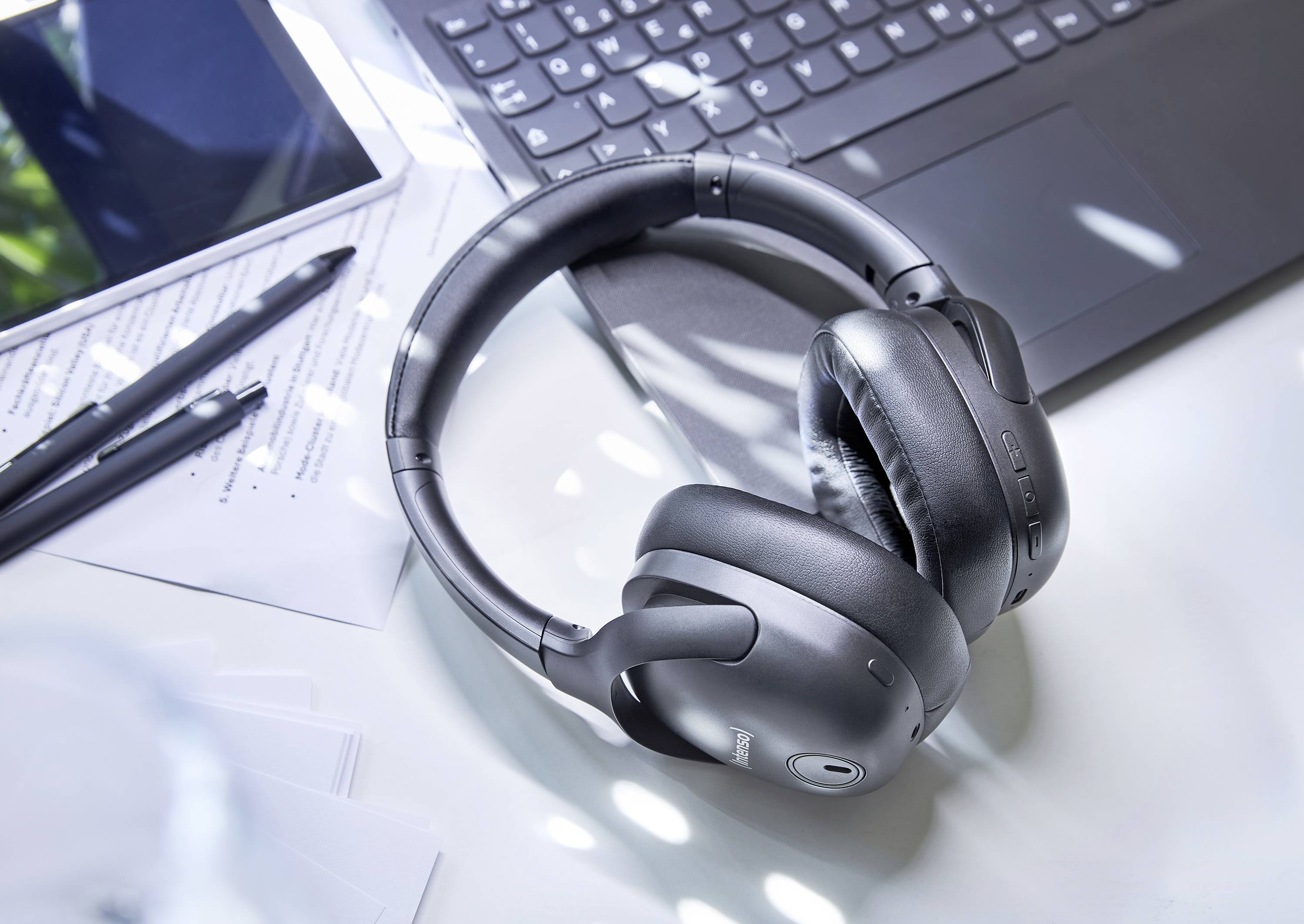 Koptelefoon ligt op een wit bureau naast een laptop, een tablet en notitiebladen met een pen.