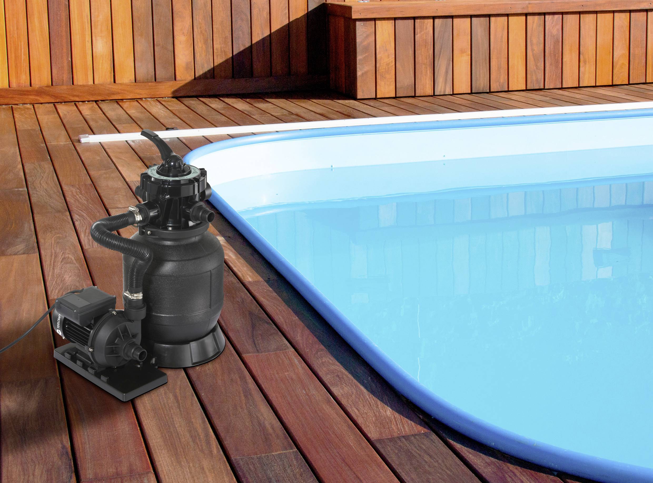 Een zwembad met blauw water, omgeven door een houten terras. Links staat een zwarte zwembadpomp, klaar voor gebruik.