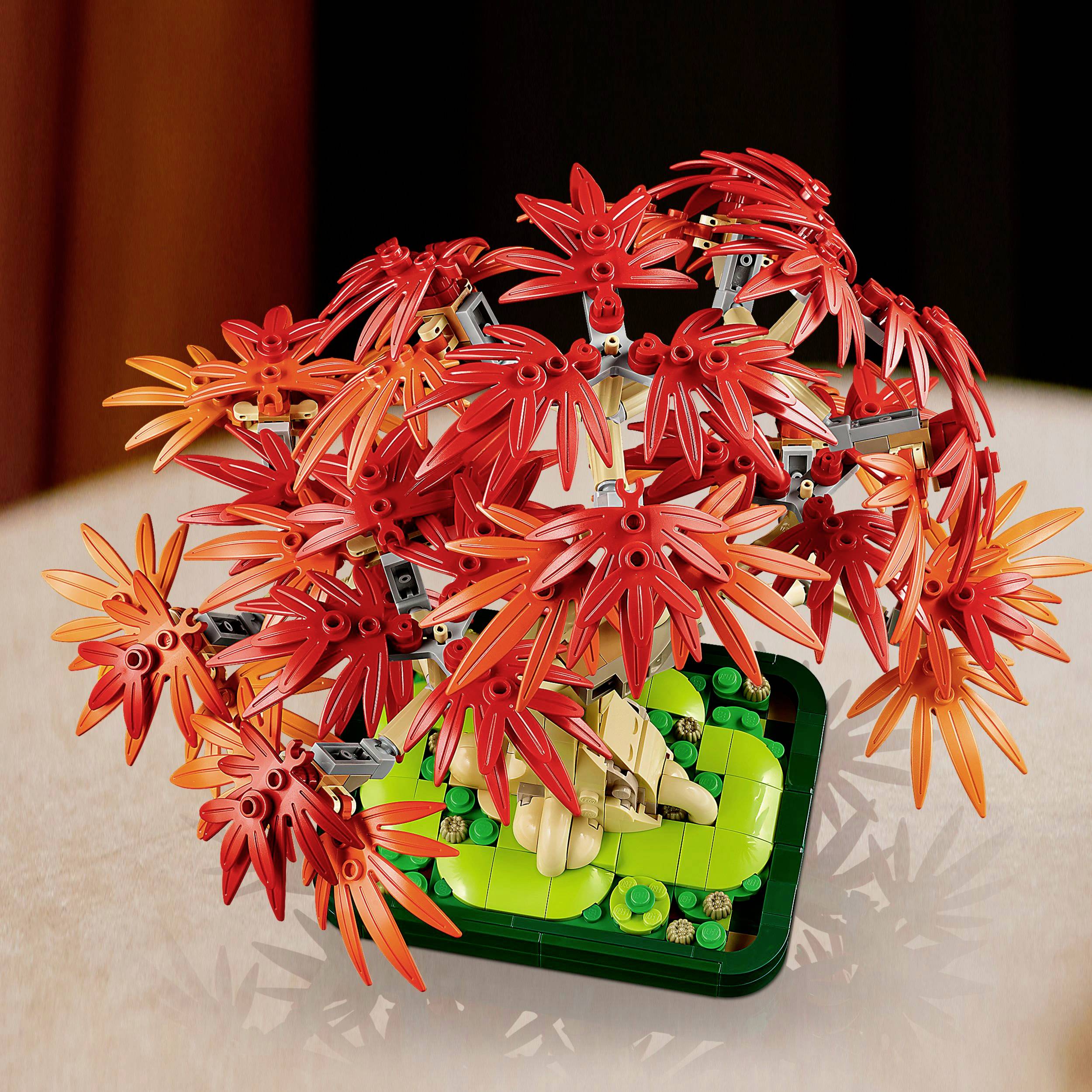 Een LEGO-boom met helderrode bladeren op een groene sokkel.