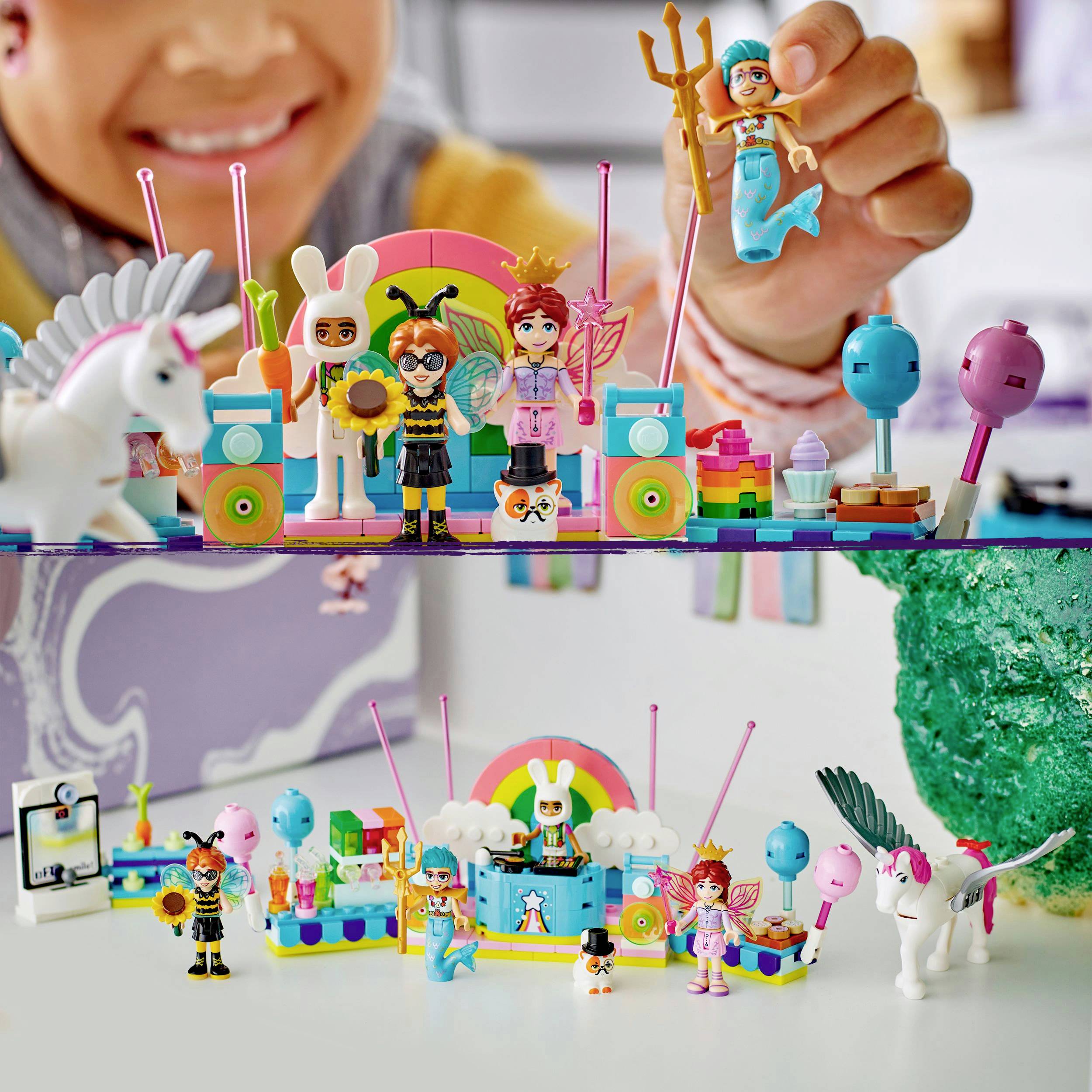 Een kind houdt een speelgoedzeemeermin vast. Daaronder een selectie kleurrijk speelgoed en accessoires zoals een eenhoorn, regenboog en ballonnen.