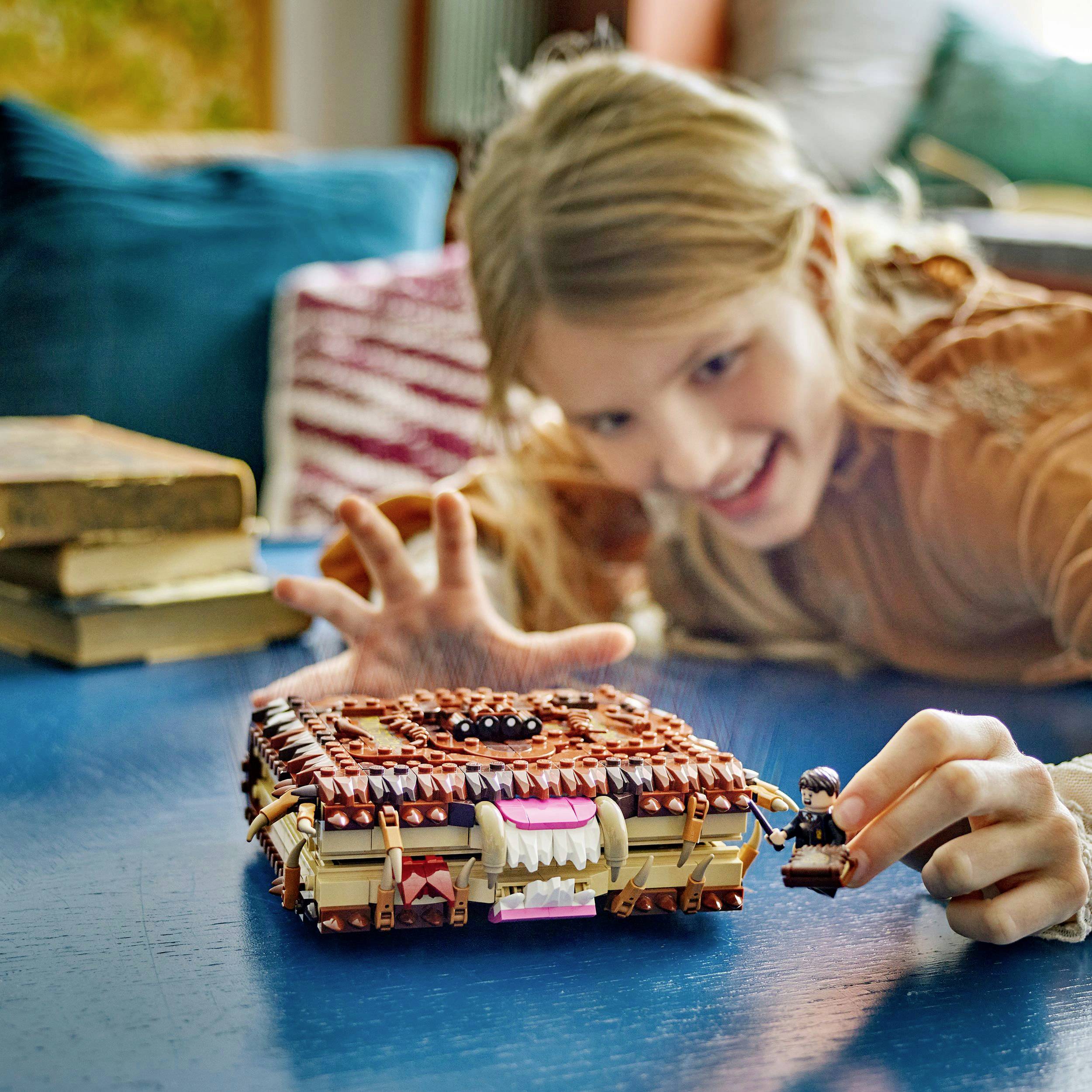 Kind speelt met miniatuurfiguur naast gedetailleerde, kubusachtige doos met gezicht en tanden op blauwe tafel.