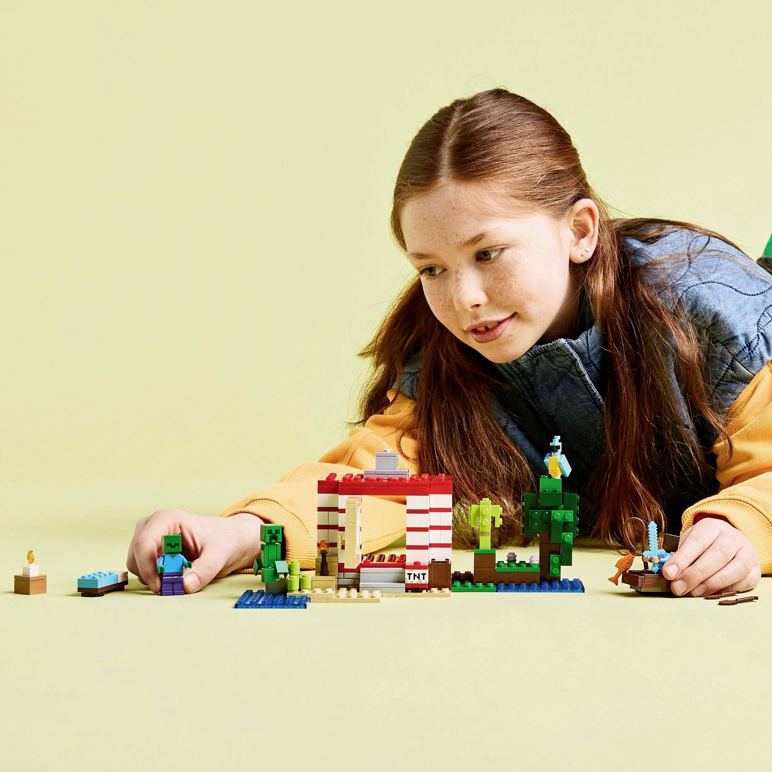 Een kind speelt met Minecraft-LEGO-stenen op een gele achtergrond. Het concentreert zich op het bouwen van structuren.
