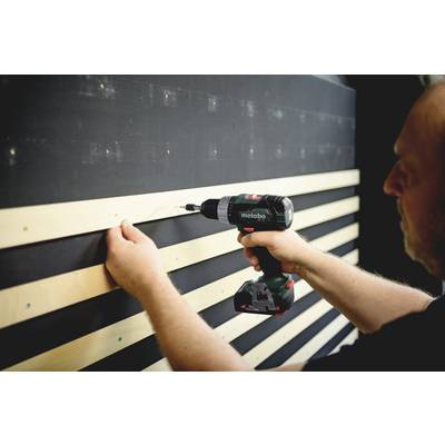 Een persoon bevestigt houten latten aan een zwarte muur met een accuboormachine.