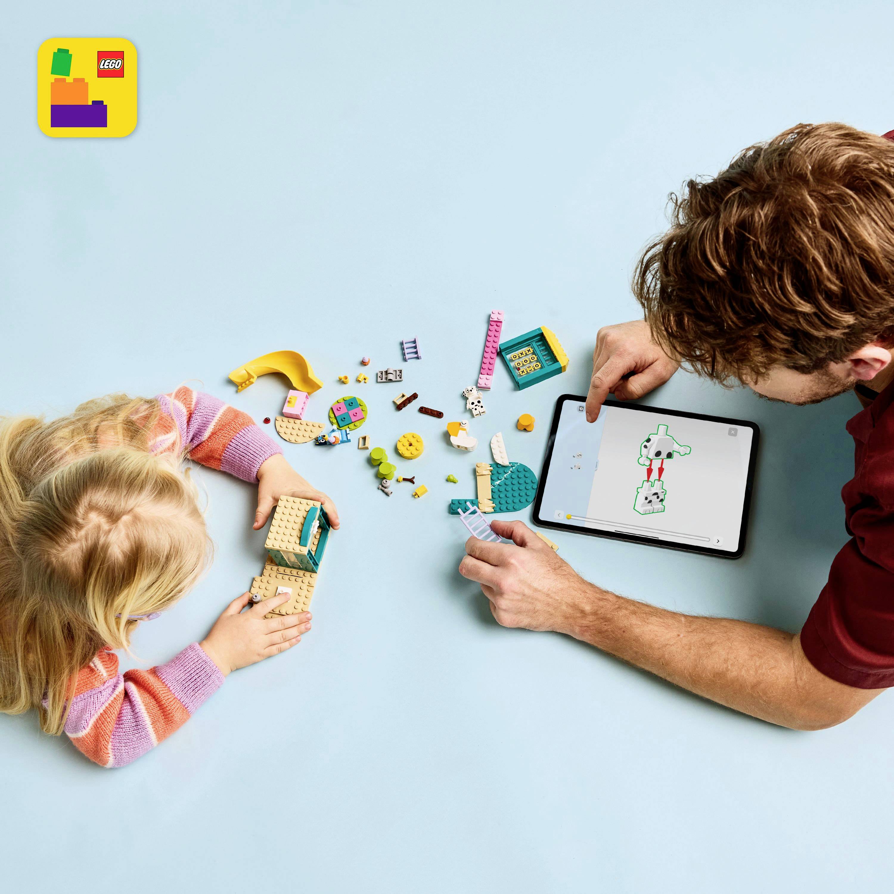 Een kind speelt met LEGO-blokken terwijl een volwassene een tablet vasthoudt waarop een LEGO-bouwhandleiding wordt weergegeven.