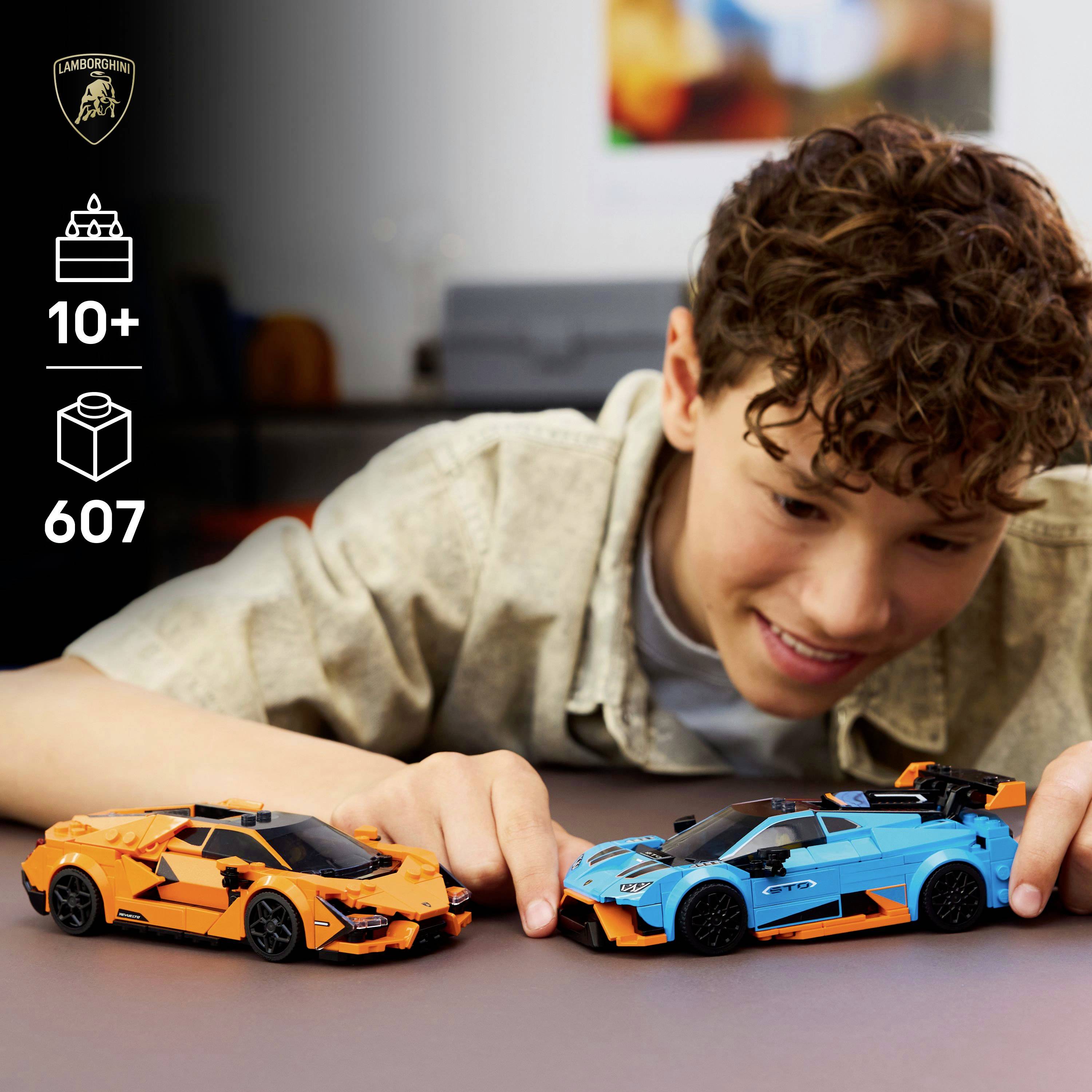Een kind lacht terwijl het speelt met twee Lamborghini modelauto's, één oranje en één blauw, in een kamer. De afbeelding toont het Lamborghini-logo en speelgoeddetails zoals '10+', '607'.