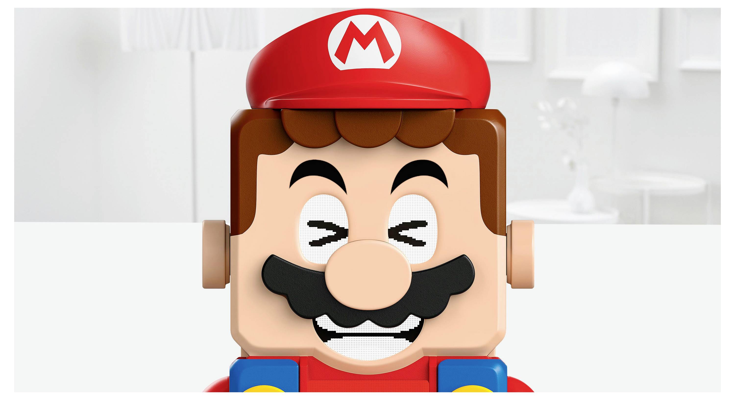 Een blokkerig speelfiguurtje met een rode hoed met een 'M'-markering, gelijkend op een klassiek videospersonage, glimlachend met gesloten ogen, in een neutrale omgeving.