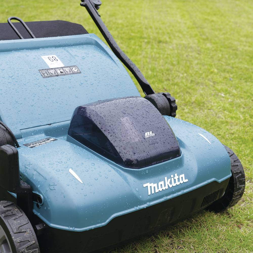 Grasmaaier van het merk Makita op een groene weide, bedekt met waterdruppels, staat klaar voor gebruik.