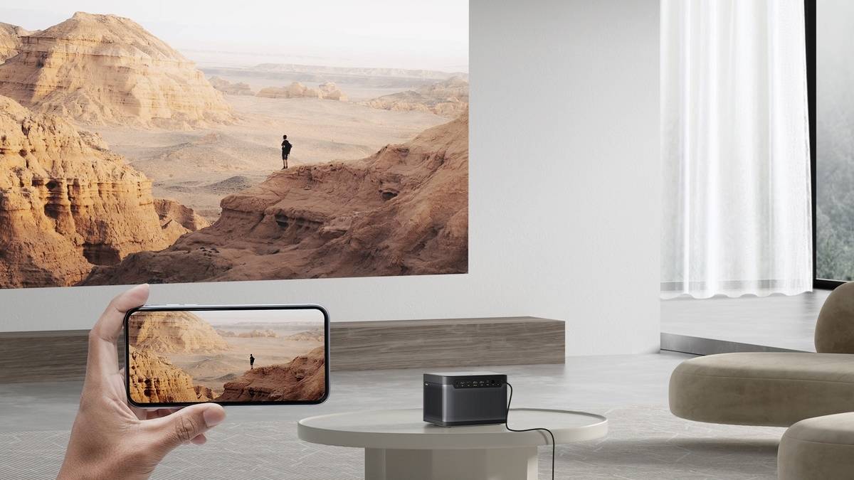 Een hand houdt een smartphone vast waarop een afbeelding van een woestijnlandschap wordt getoond, terwijl dit beeld op een muur wordt geprojecteerd.