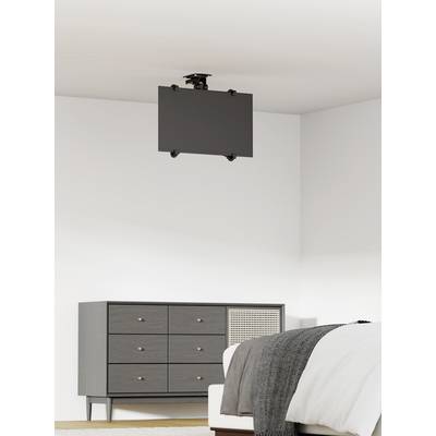 Een grijze ruimte toont een ladenkast links en een bed rechts. Aan het plafond hangt een flatscreen.