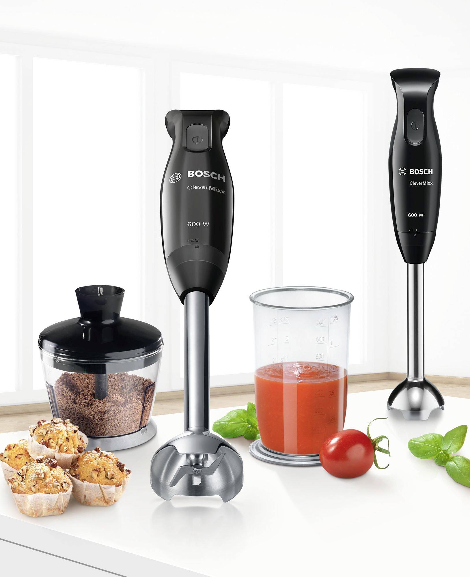 'Twee zwarte Bosch staafmixers van 600 Watt voor een raam met een transparante maatbeker, gehakte noten en tomatensaus.'