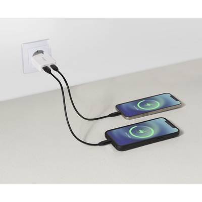 Twee smartphones op een tafel aangesloten op een wandadapter, waarbij beide toestellen een groen oplaadsymbool op hun schermen tonen, wat actief opladen aangeeft.