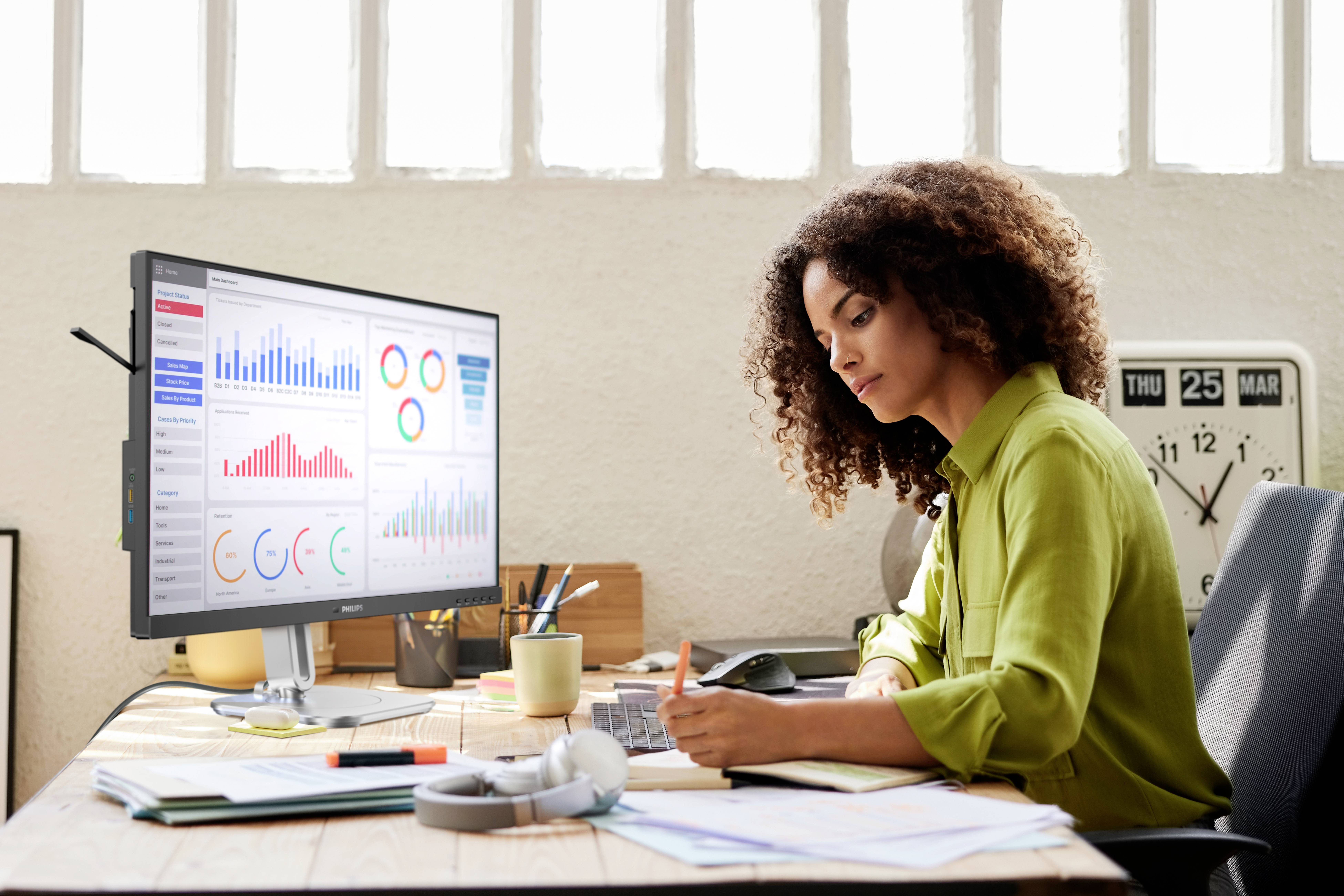 Een vrouw werkt aan een bureau met een computer die verschillende gekleurde grafieken en diagrammen weergeeft.