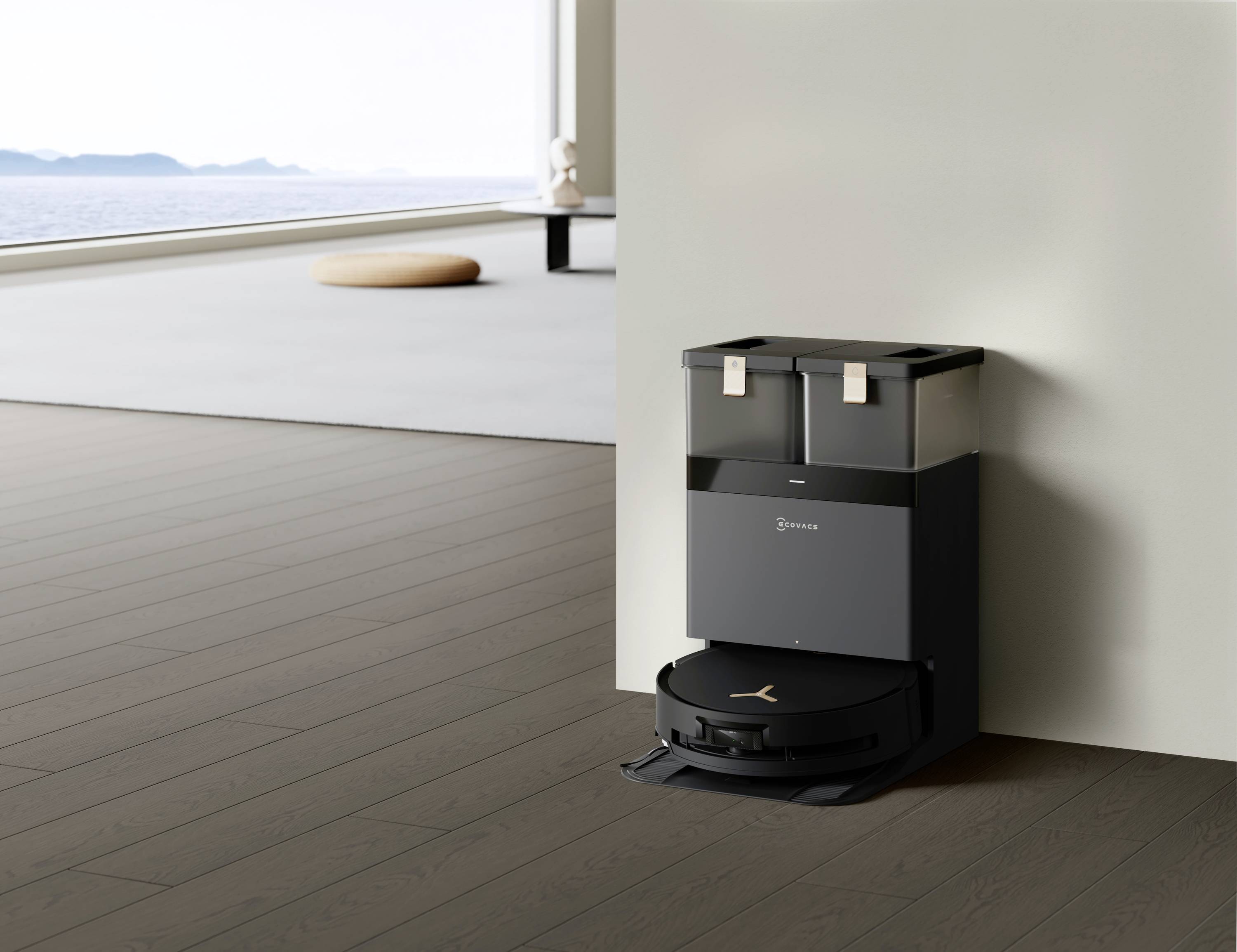 Een zwarte robotstofzuiger laadt op een station in een moderne woninghoek. Grote ramen bieden uitzicht op de zee.