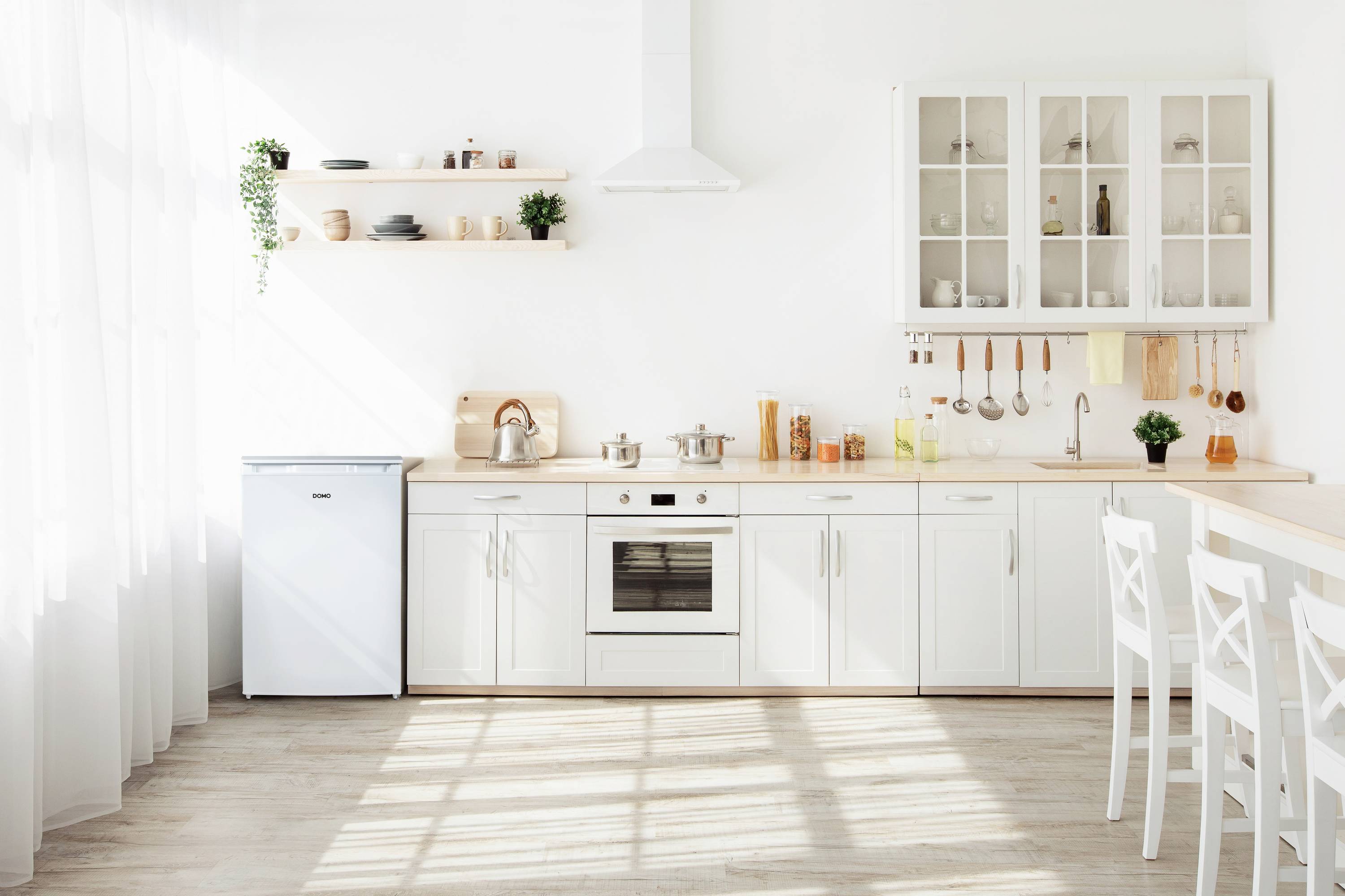 Lichte, moderne keuken met witte kasten, kleine koelkast, fornuis en planken. Zonlicht valt door het raam op de vloer.