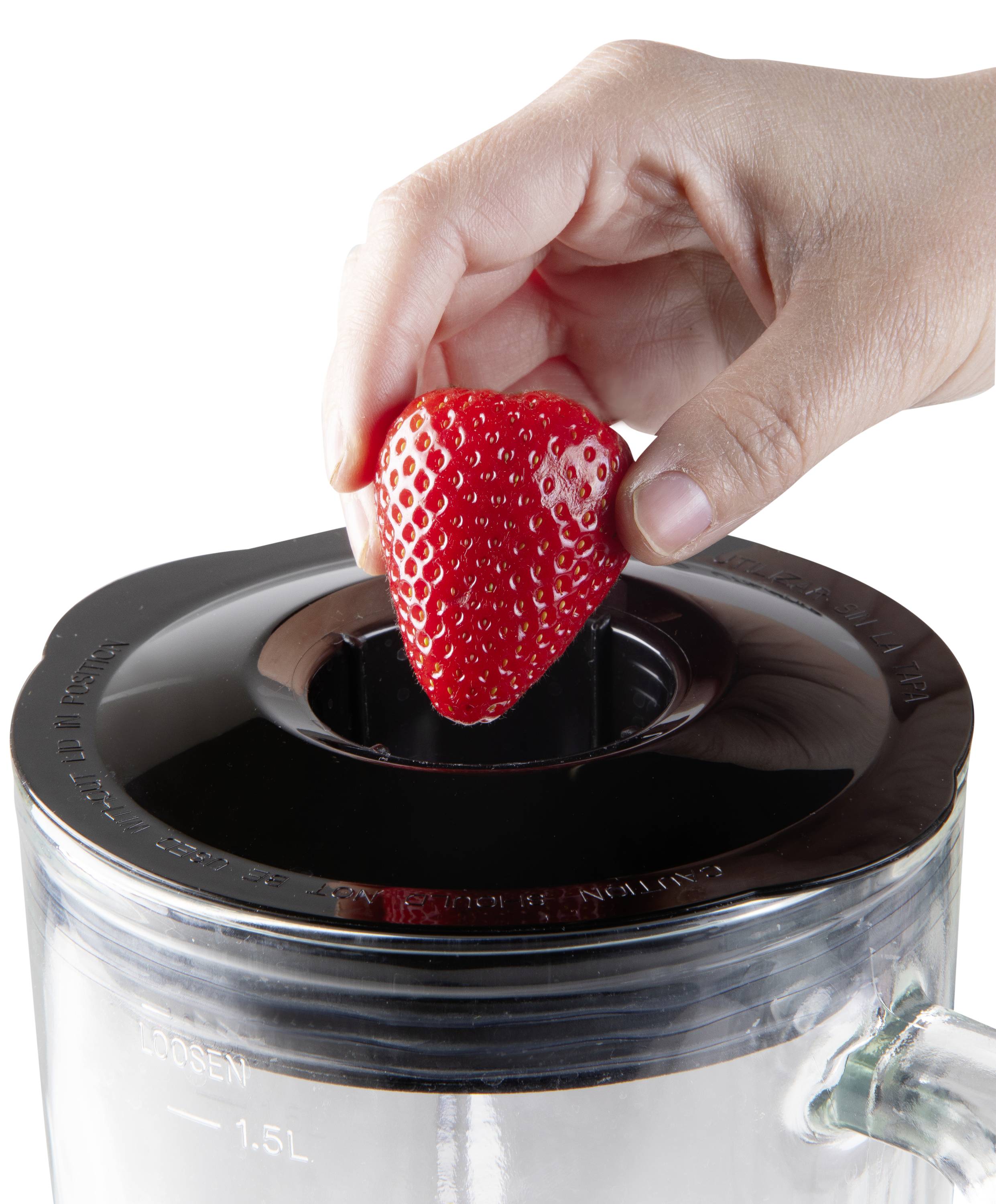 Een hand legt een aardbei in een blender.