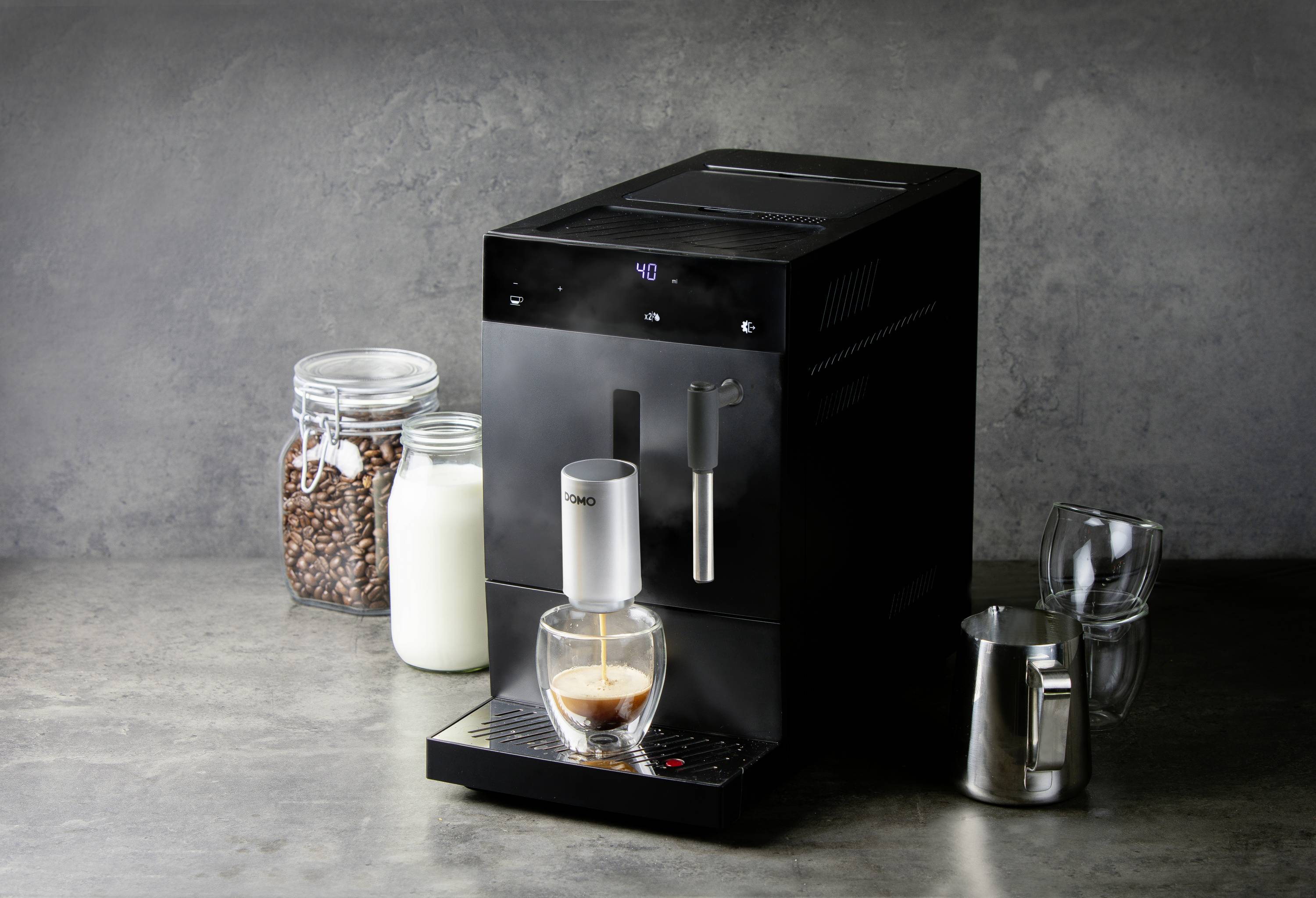 Een zwarte koffiemachine bereidt een espresso in een glas. Ernaast staan een container met koffiebonen en een melkglas.