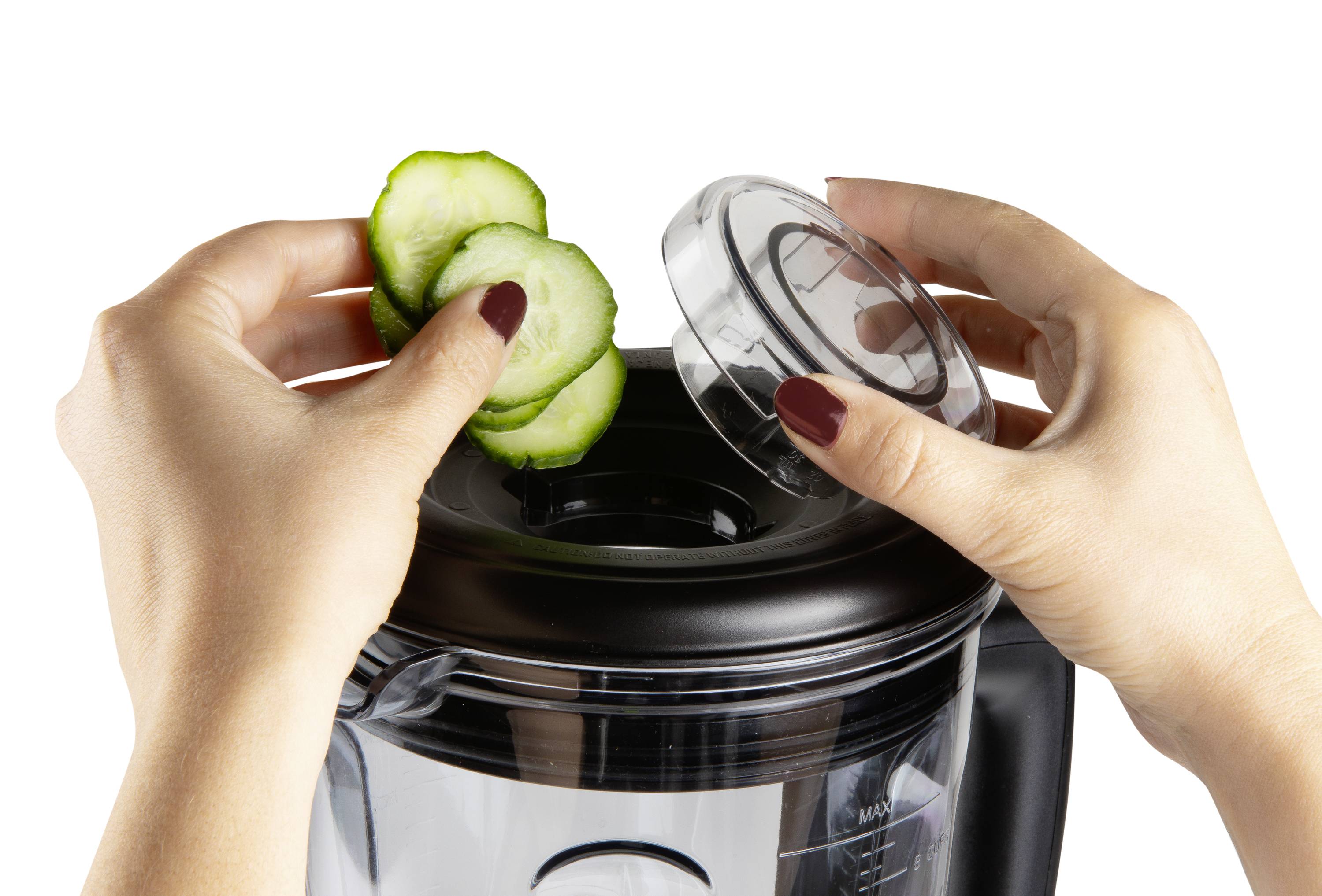 Een persoon legt komkommerschijfjes in een blender, waarvan het deksel in de andere hand wordt vastgehouden.
