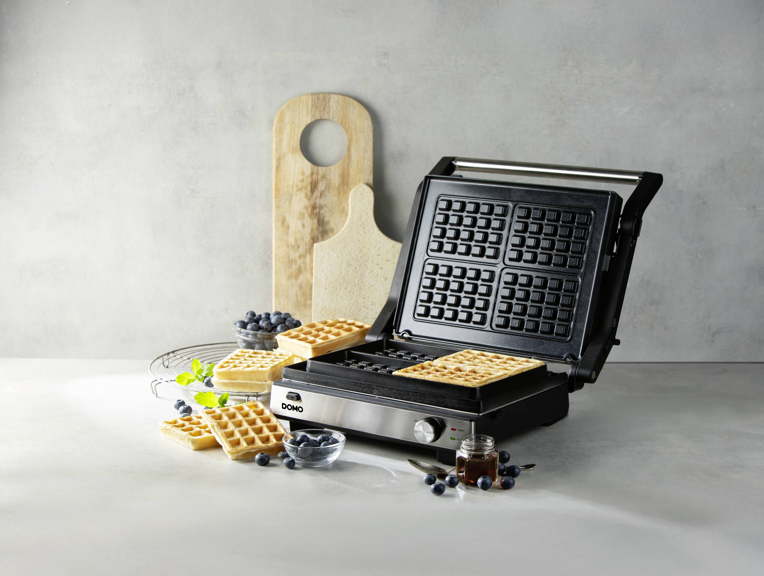 Wafelijzer in geopende positie met vers gebakken wafels, omringd door bosbessen op een lichte achtergrond.