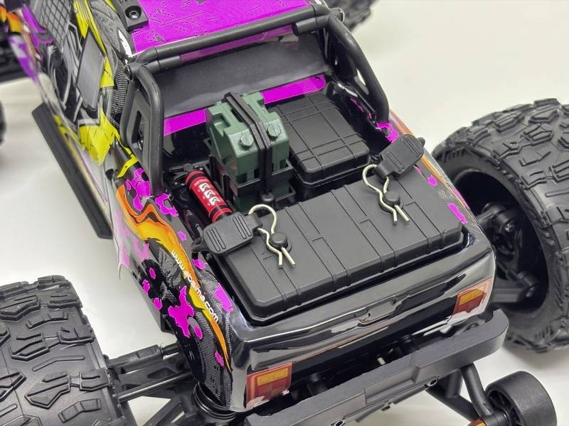 Afstandsbestuurbare auto met open laadruimte die batterijen en accessoires toont. Kleurrijke carrosserie met roze, gele en zwarte details.